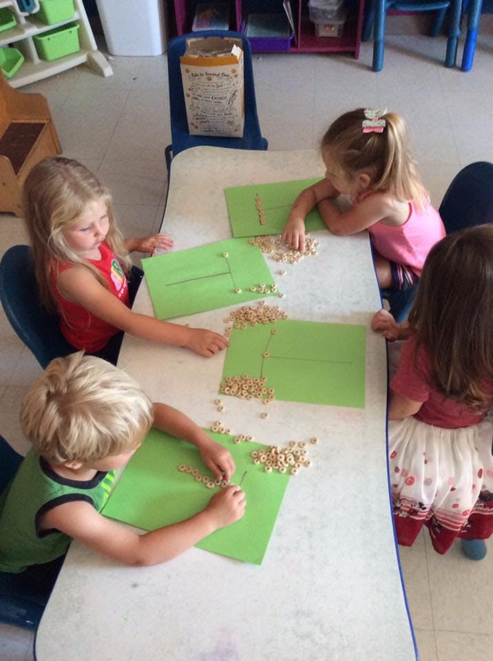 Four children at a table working with cereal pieces on green paper