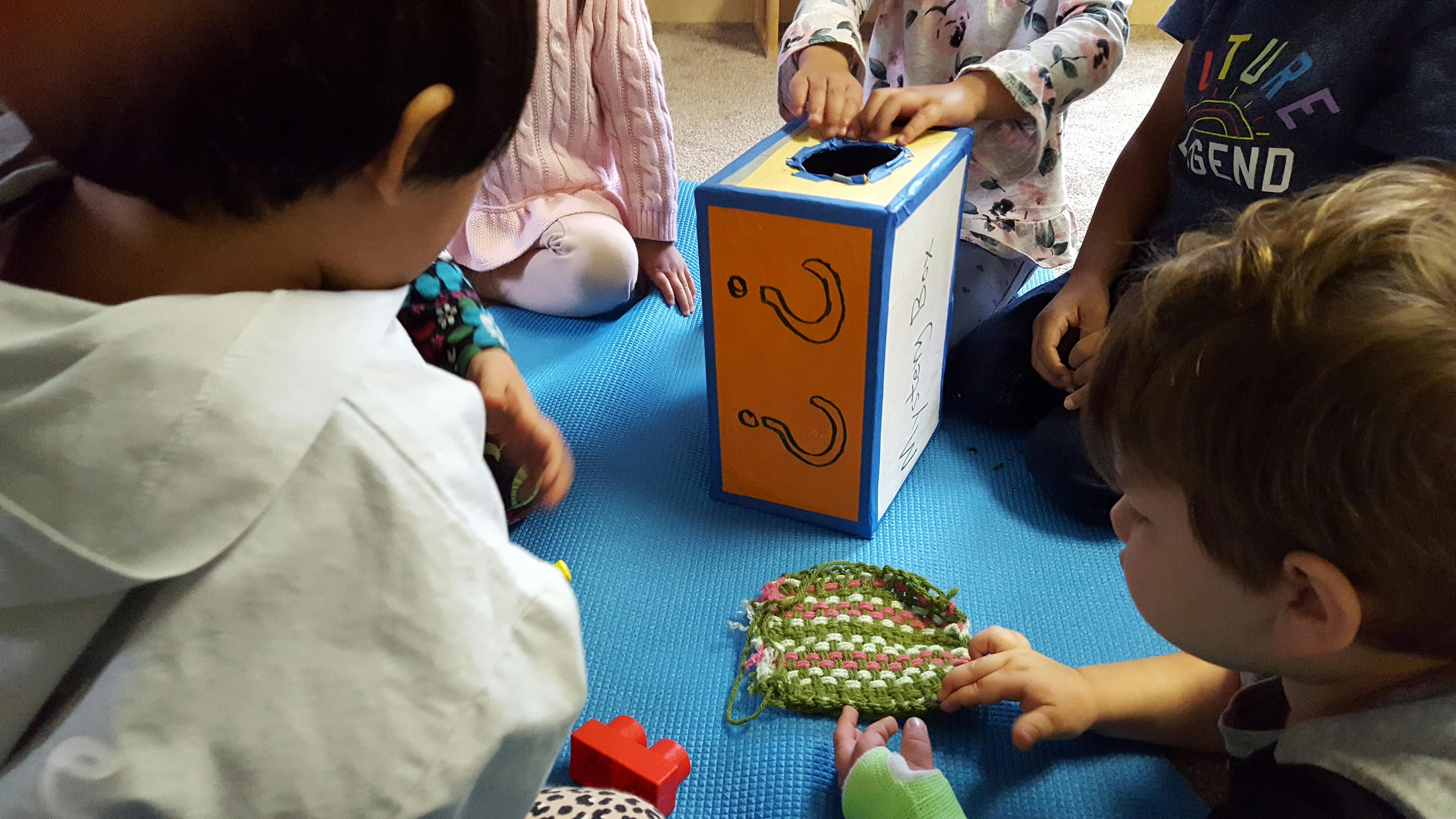 Children playing with a box and toys on a blue mat