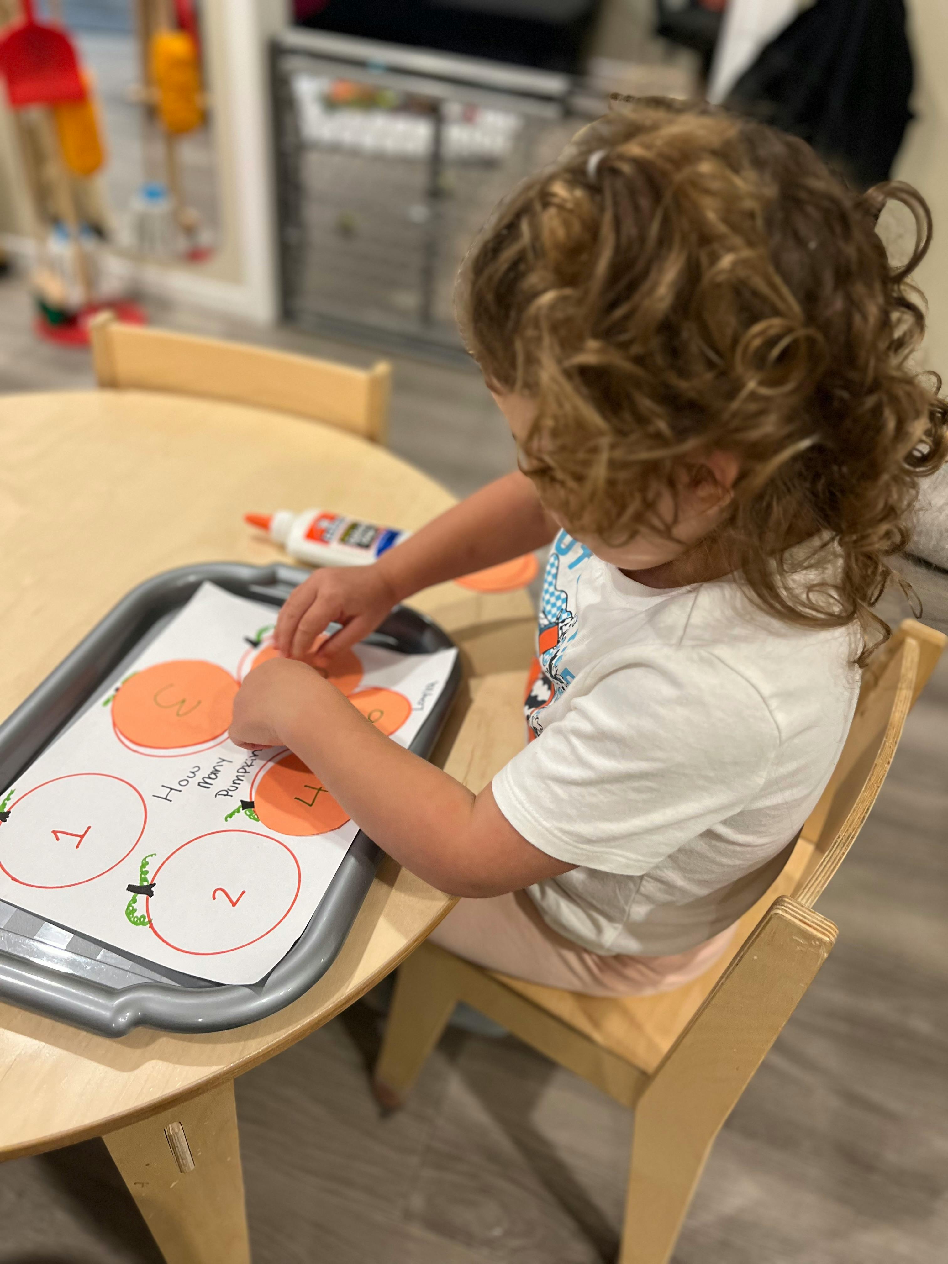 Child sitting at a table doing a craft with paper cutouts