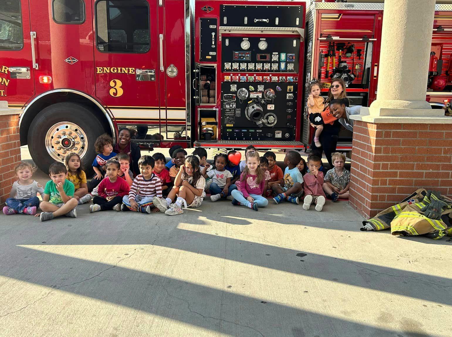 Children and adults sitting on the ground in front of a fire truck