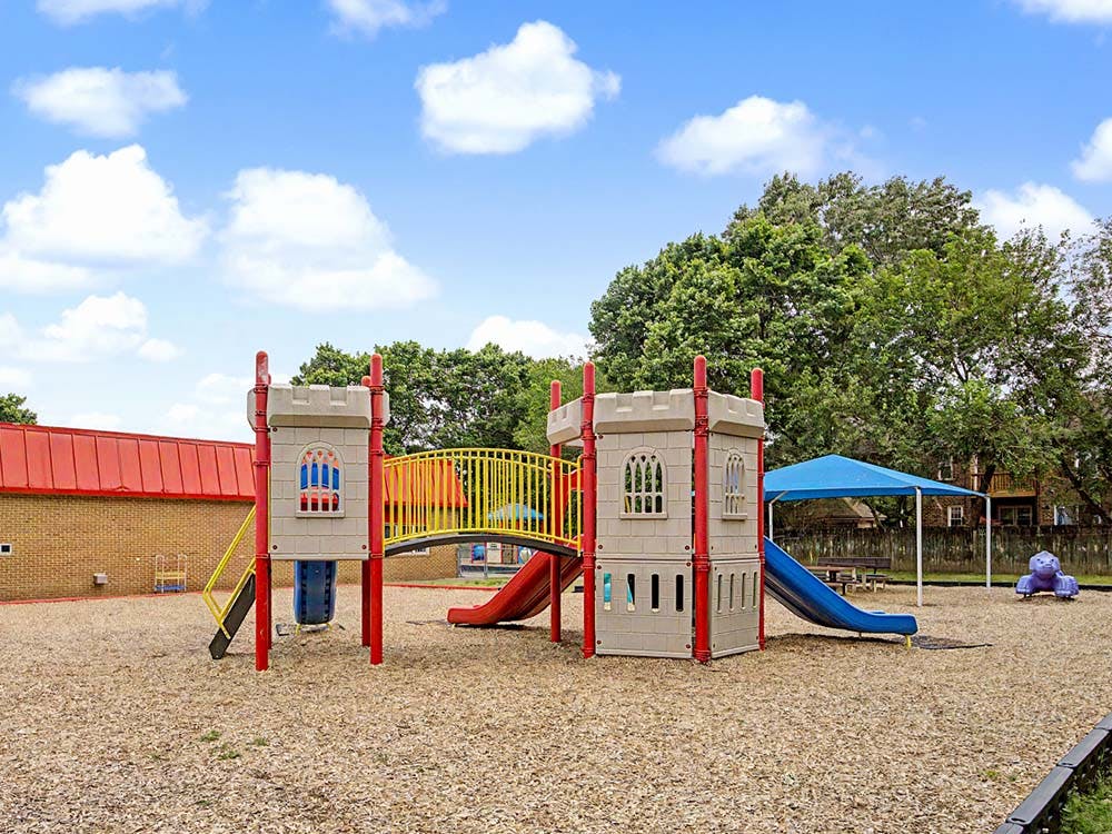 A castle-themed playground with slides and a bridge on wood chips under a blue sky