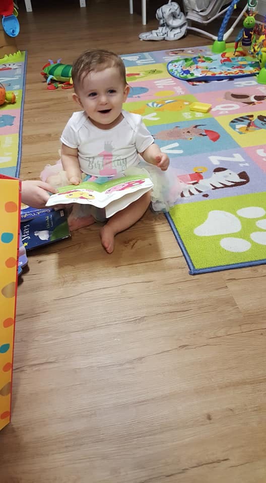 Child sitting on a playmat, holding an open book