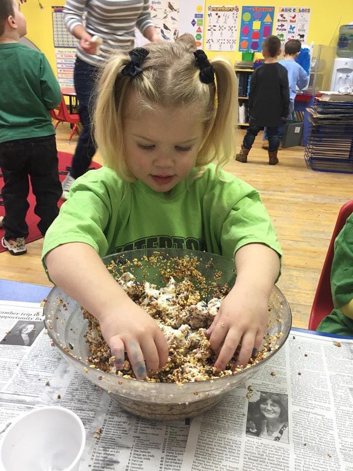 Child mixing ingredients in a large bowl in a classroom