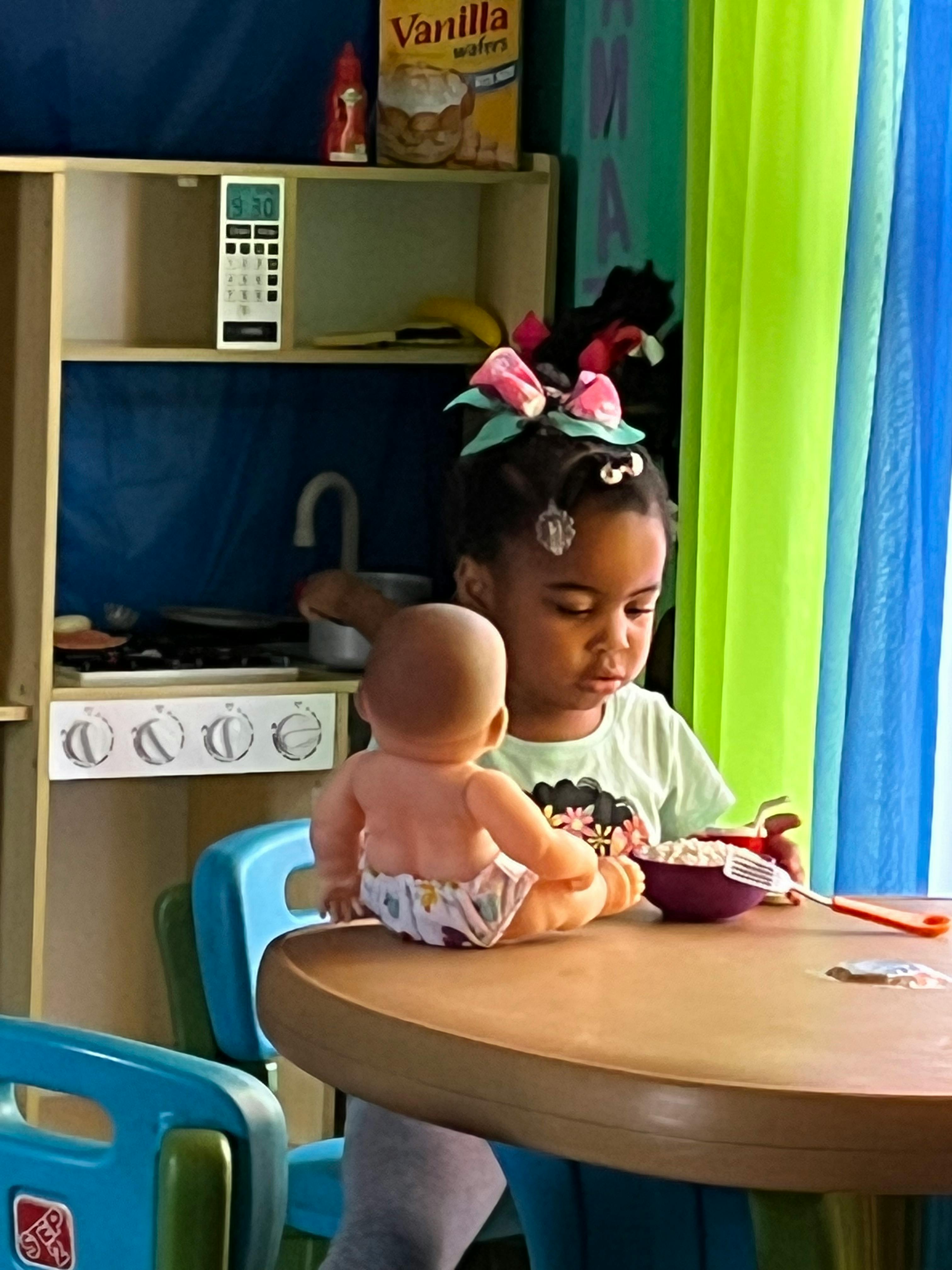 Child playing with a doll and toy food at a table