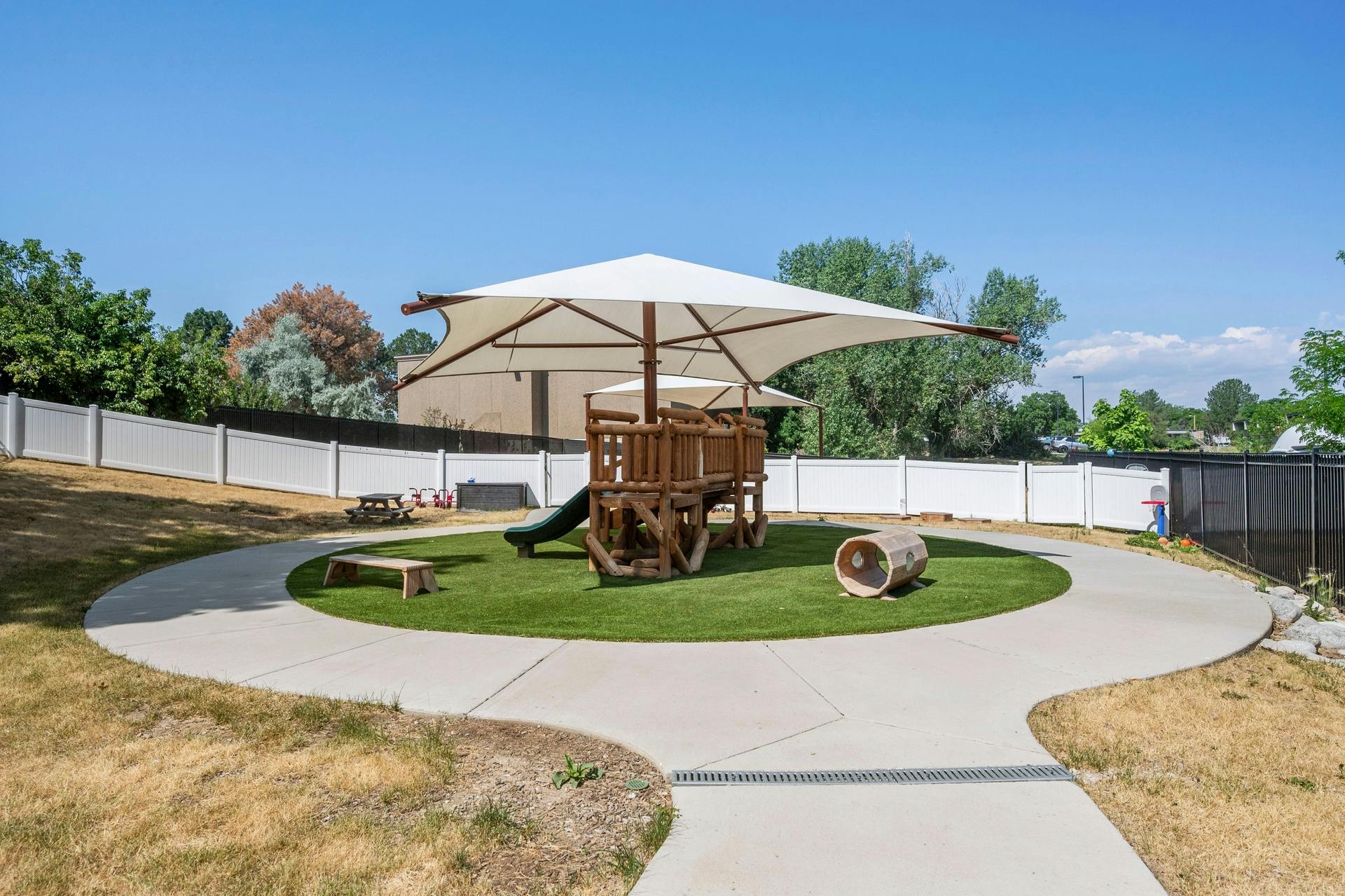 Outdoor playground with a wooden play structure and green slide under a large umbrella