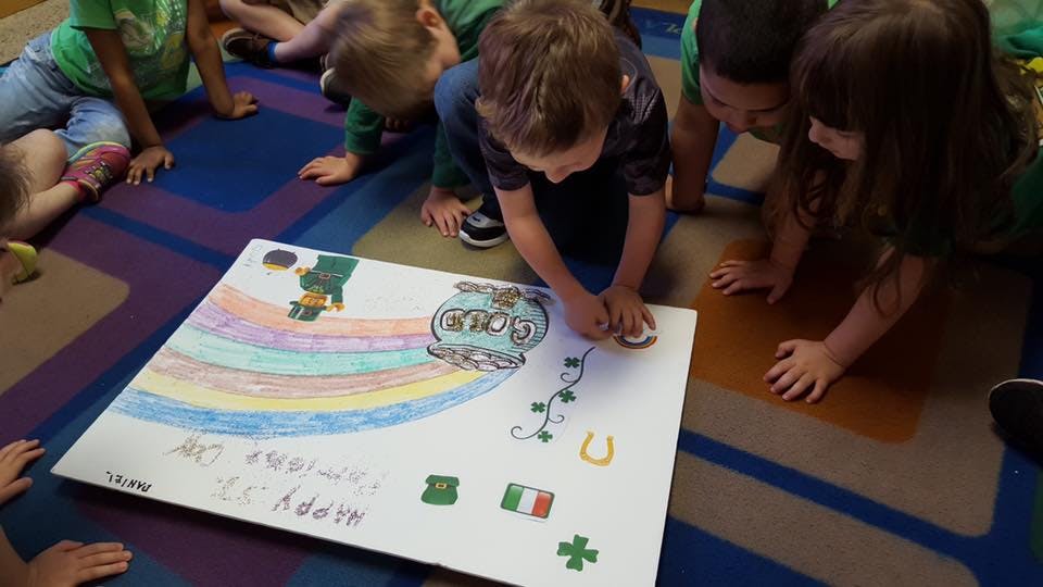 Children gathered around a poster with a rainbow and shamrocks