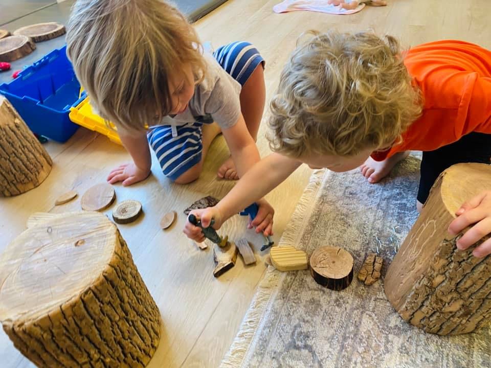 Two children playing with wooden blocks and tree stumps on the floor