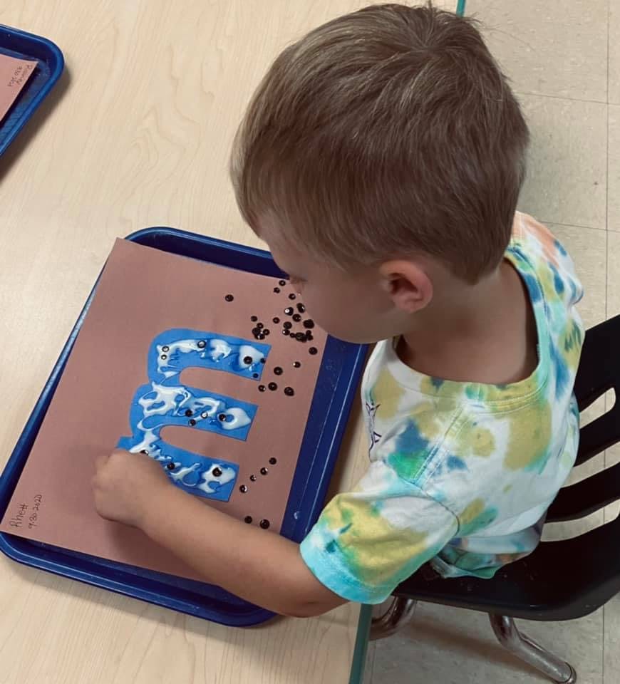 Child working on a craft project with a blue letter E and small black dots
