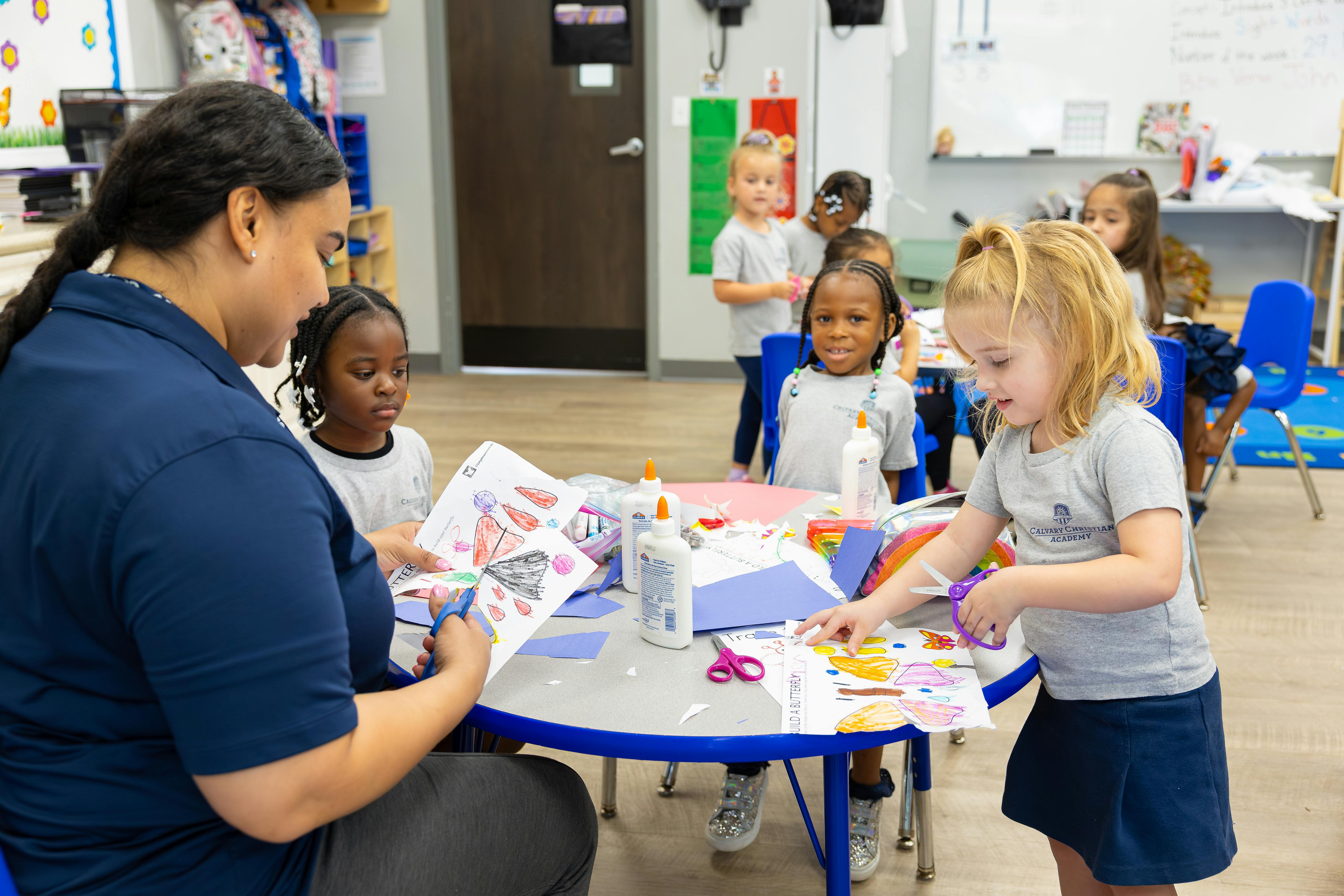 Adult and children at a table cutting paper with scissors in a classroom
