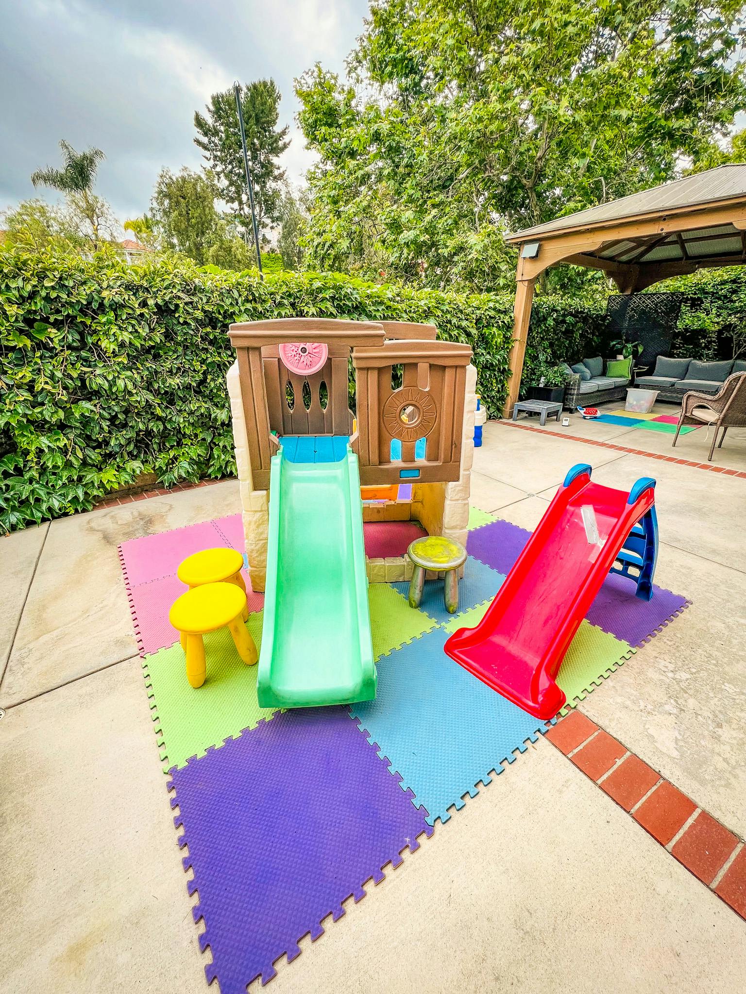 Outdoor play area with a playhouse, two slides, and colorful foam mats