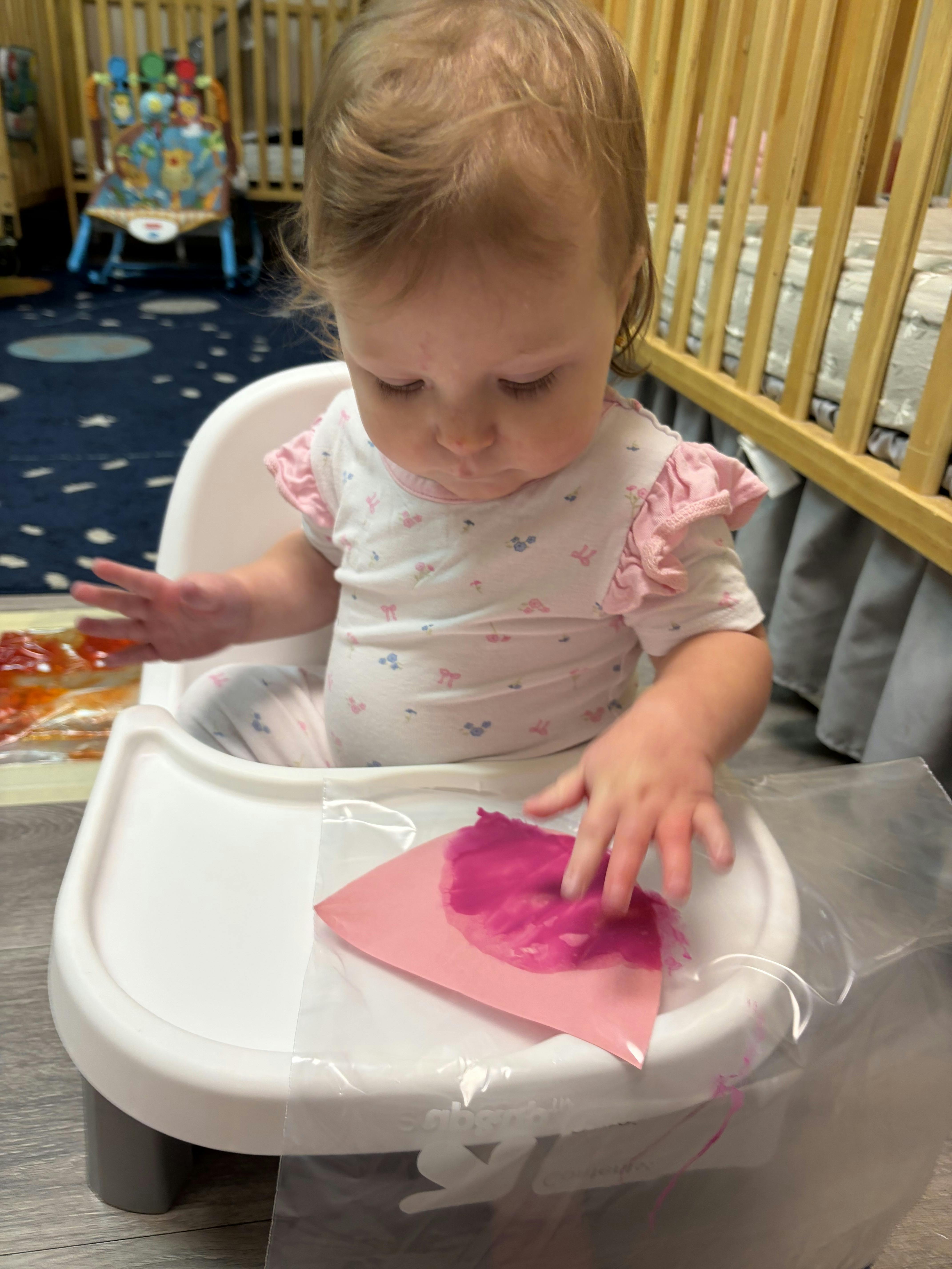 Child sitting in a high chair playing with paint inside a plastic bag