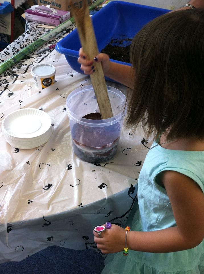 Child stirring a mixture in a clear container with a wooden stick
