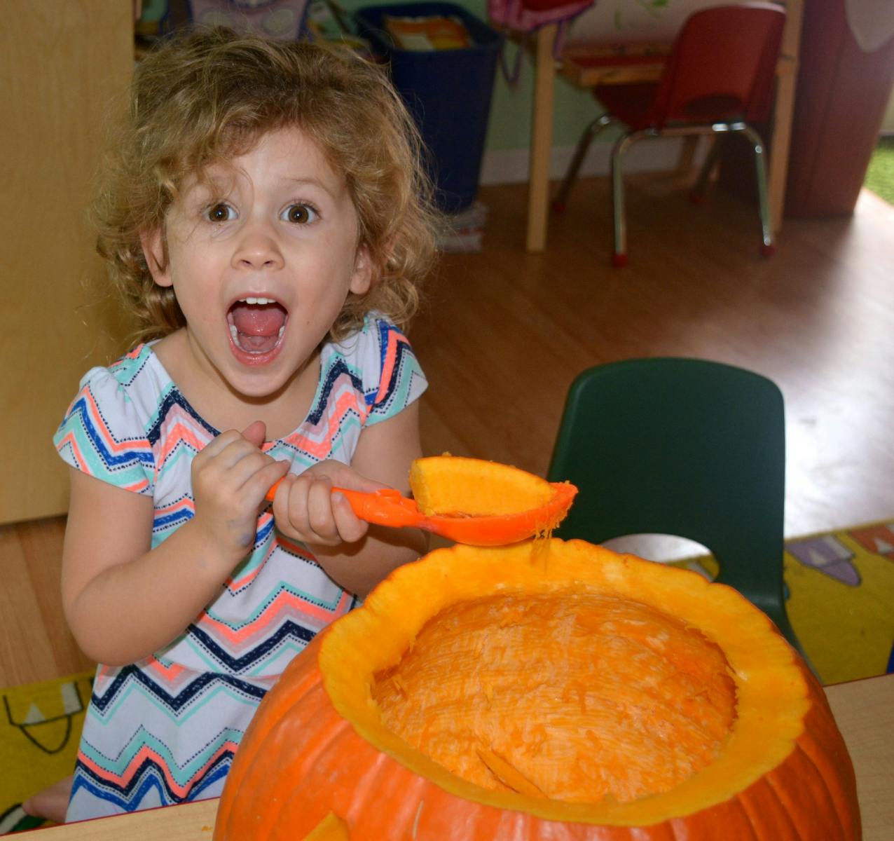 Child with open mouth holding a scoop over a pumpkin