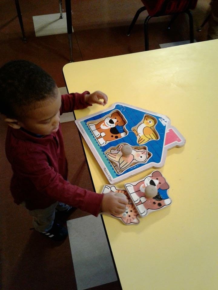 Child playing with a wooden animal puzzle on a yellow table