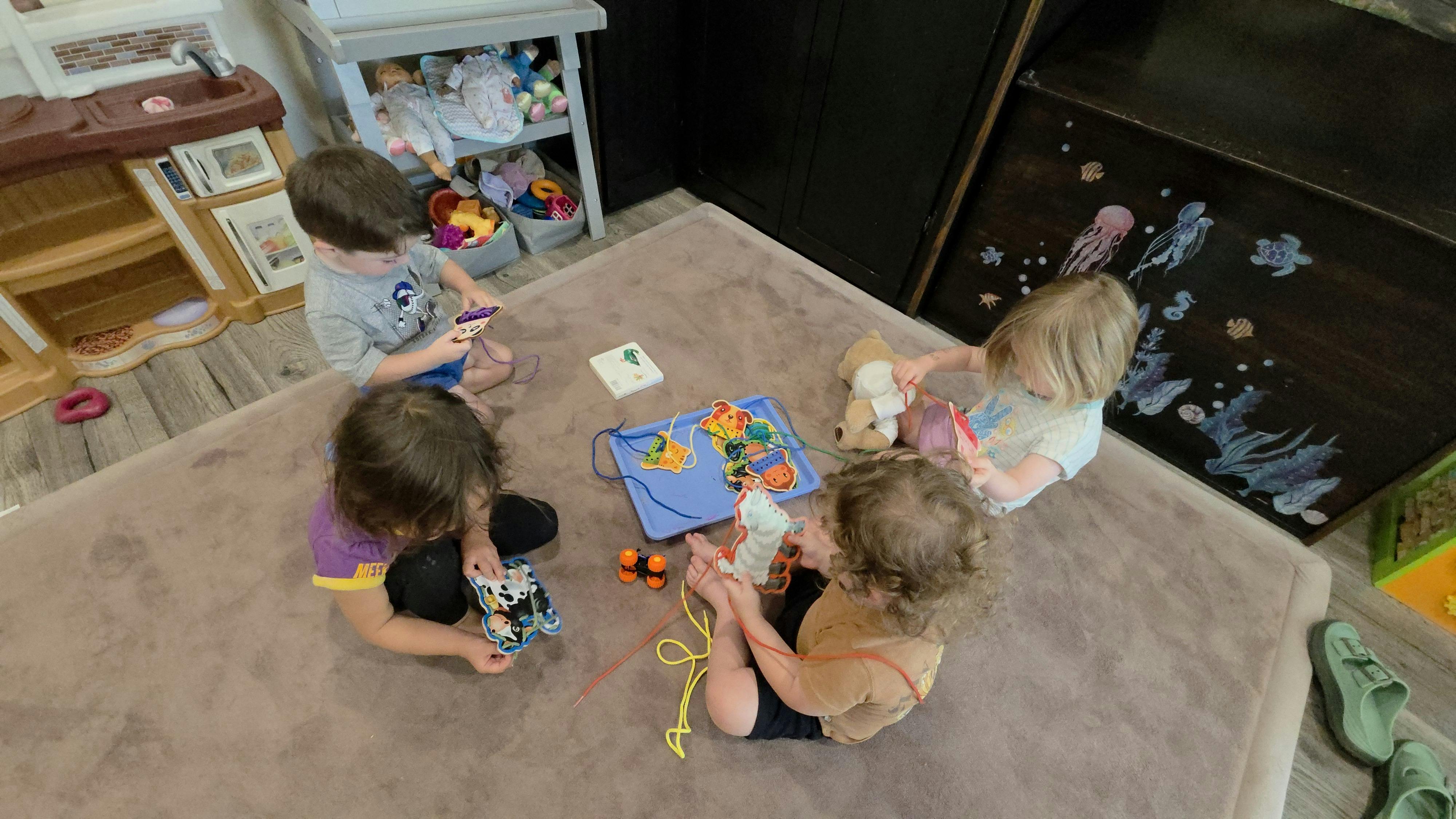 Four children sitting on a rug playing with lacing toys
