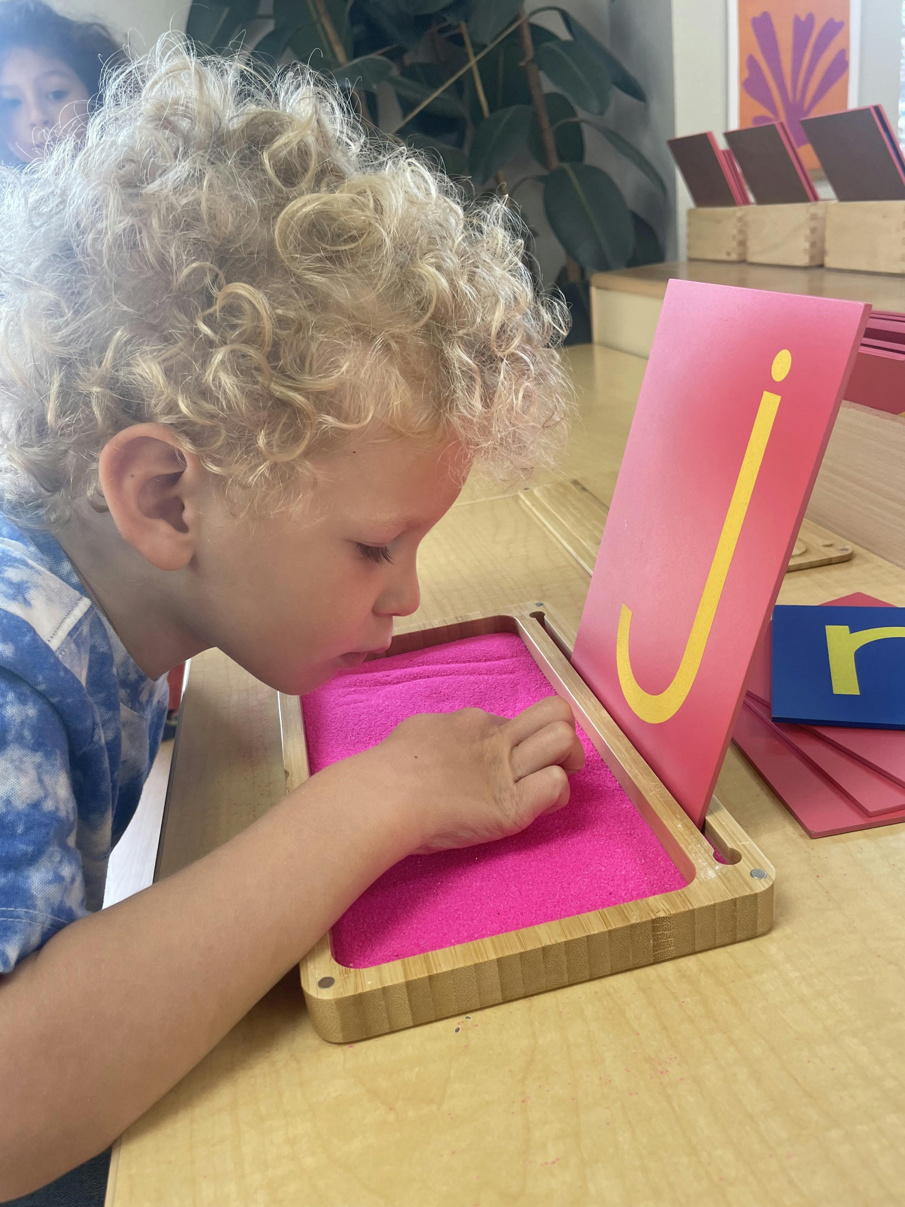 Child tracing the letter J in a sand tray