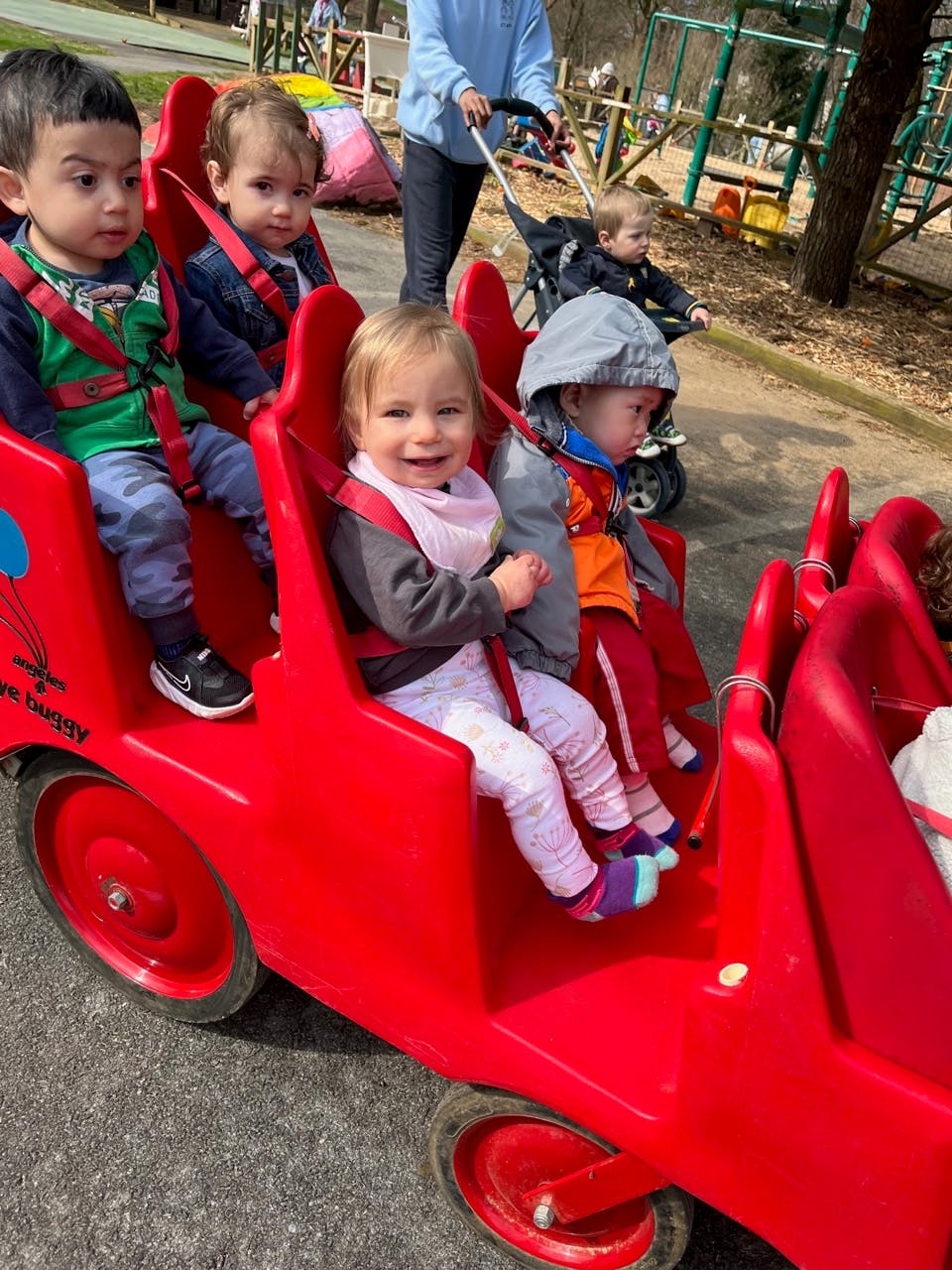 Children riding in a red wagon train-seated wagon being pulled by a person