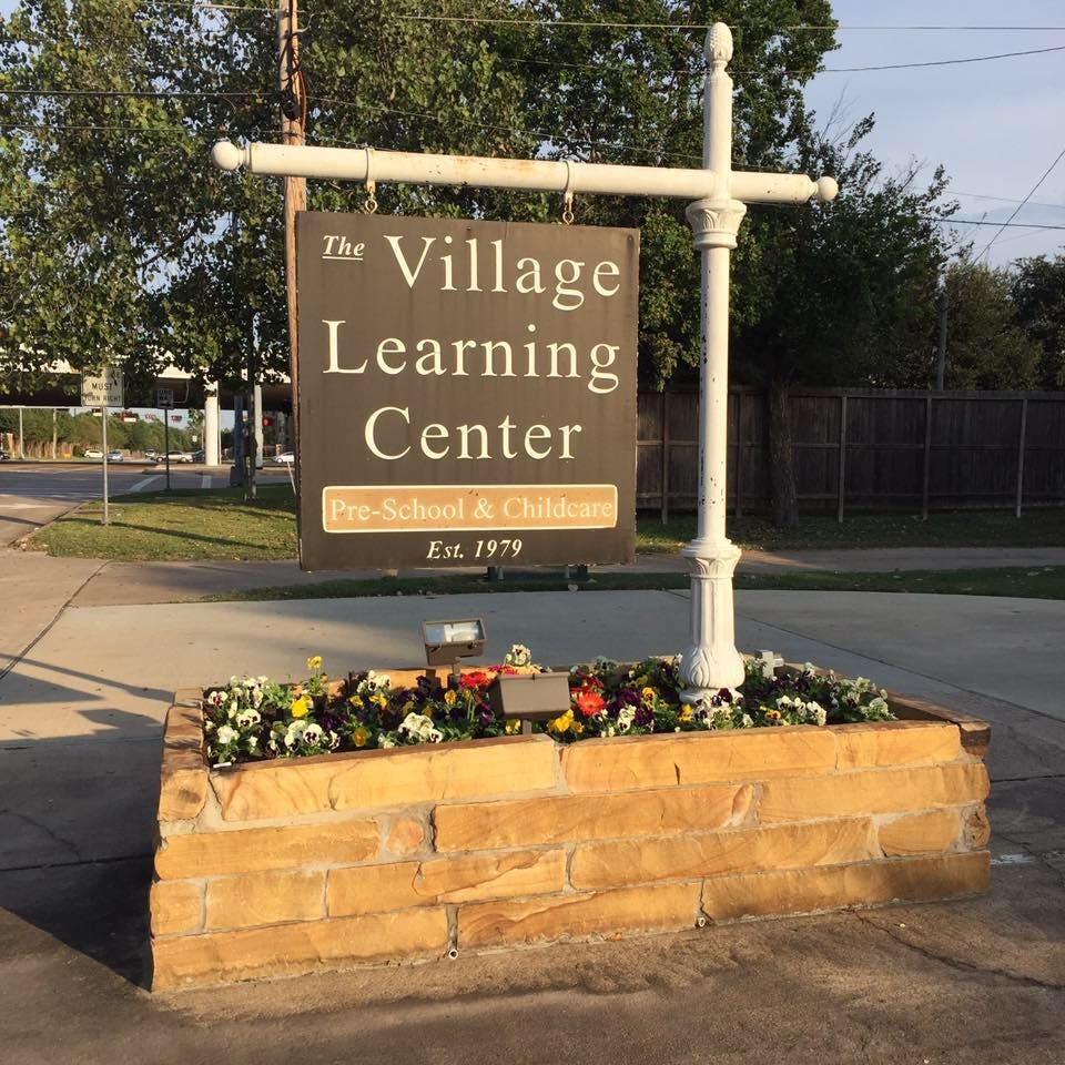 Sign for The Village Learning Center with flowers in a stone planter