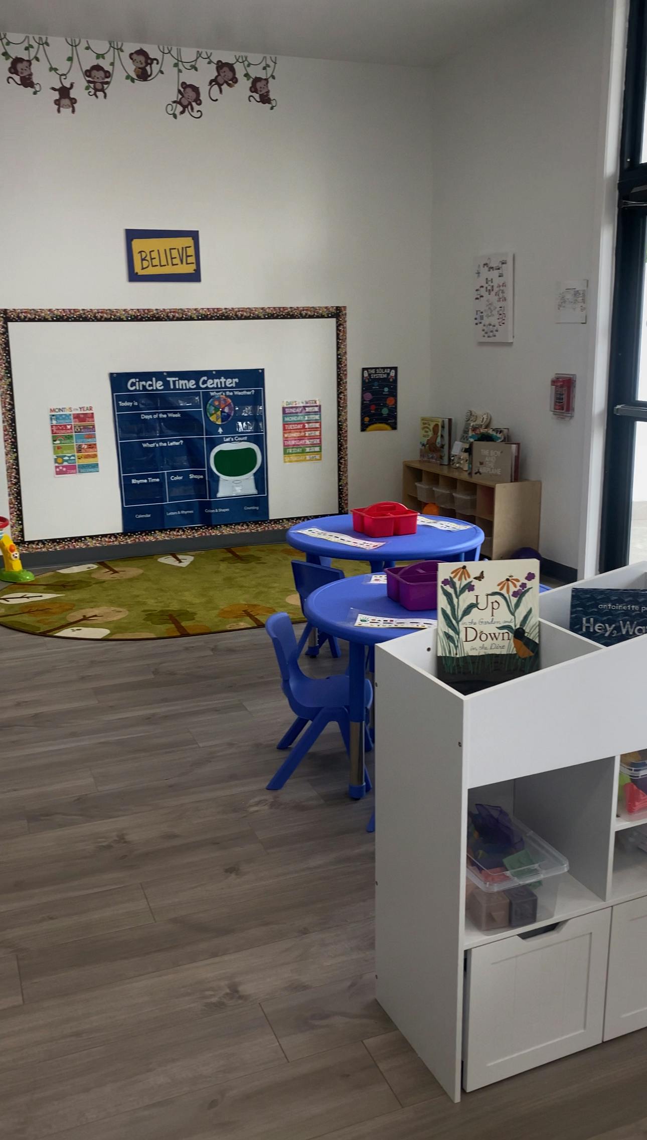Classroom with blue tables and chairs, a whiteboard, and a rug