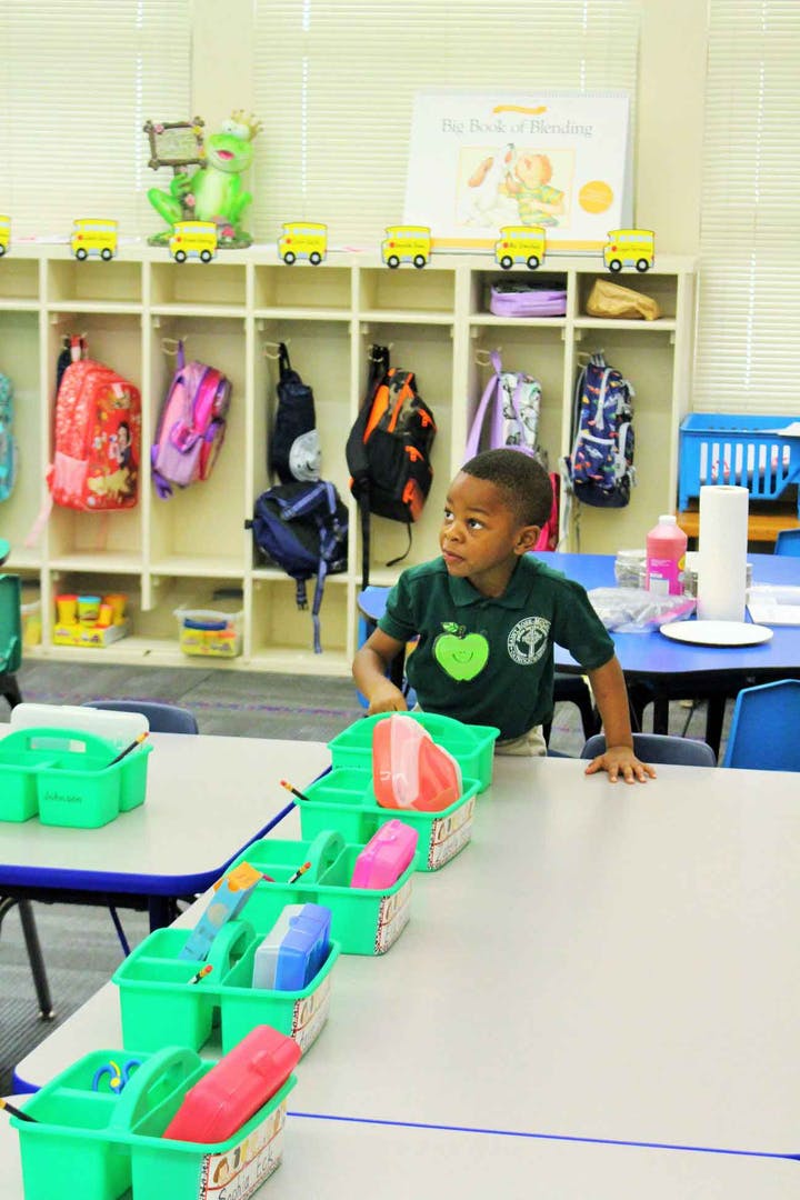 Child standing at a table in a classroom