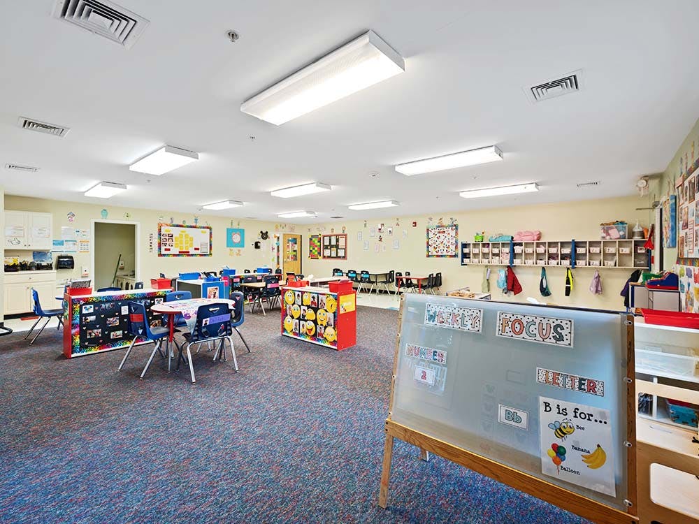 Empty classroom with small tables and chairs, cubbies, and an easel with learning materials