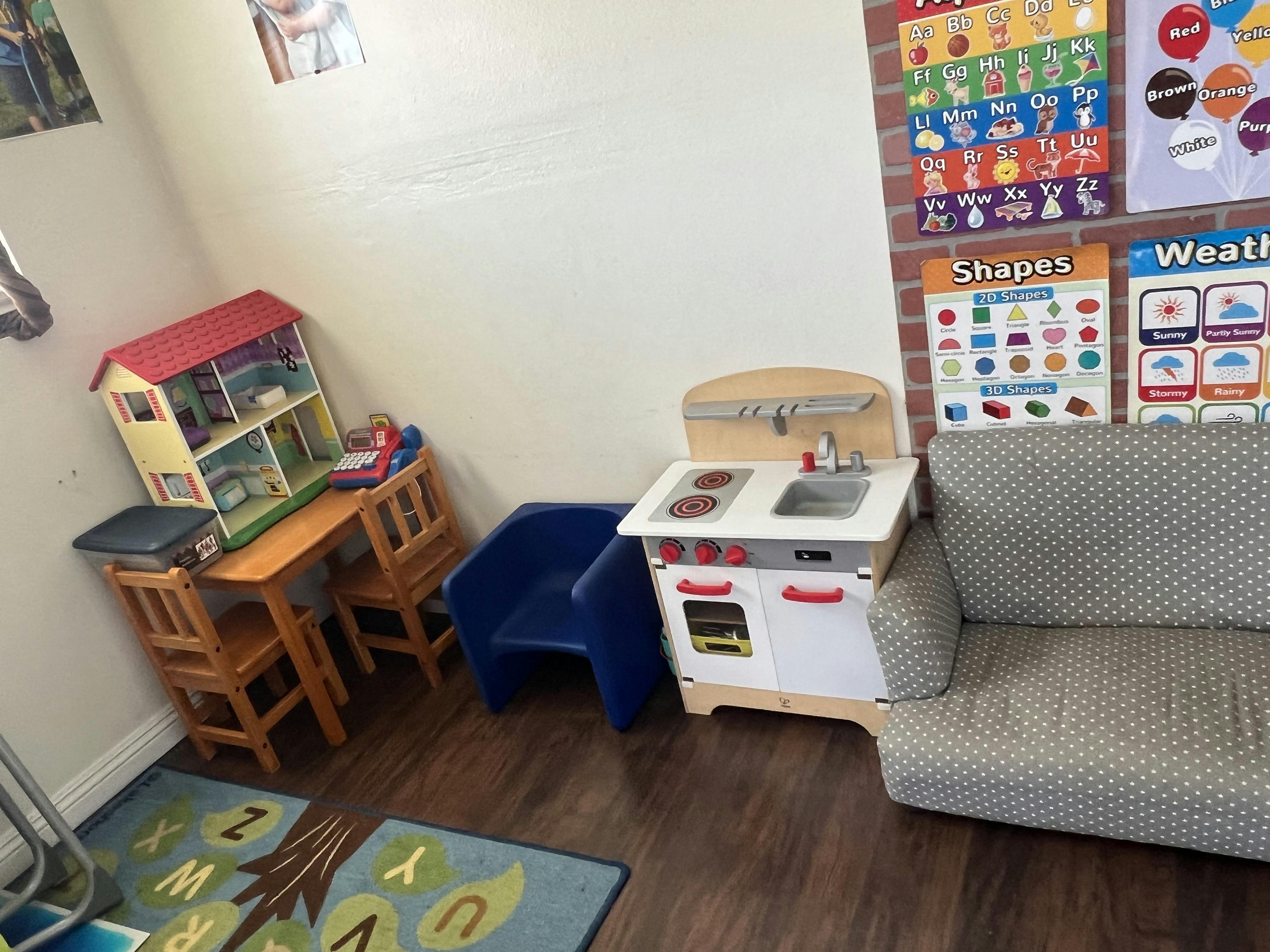 Play area with toy kitchen, dollhouse, and furniture in a classroom