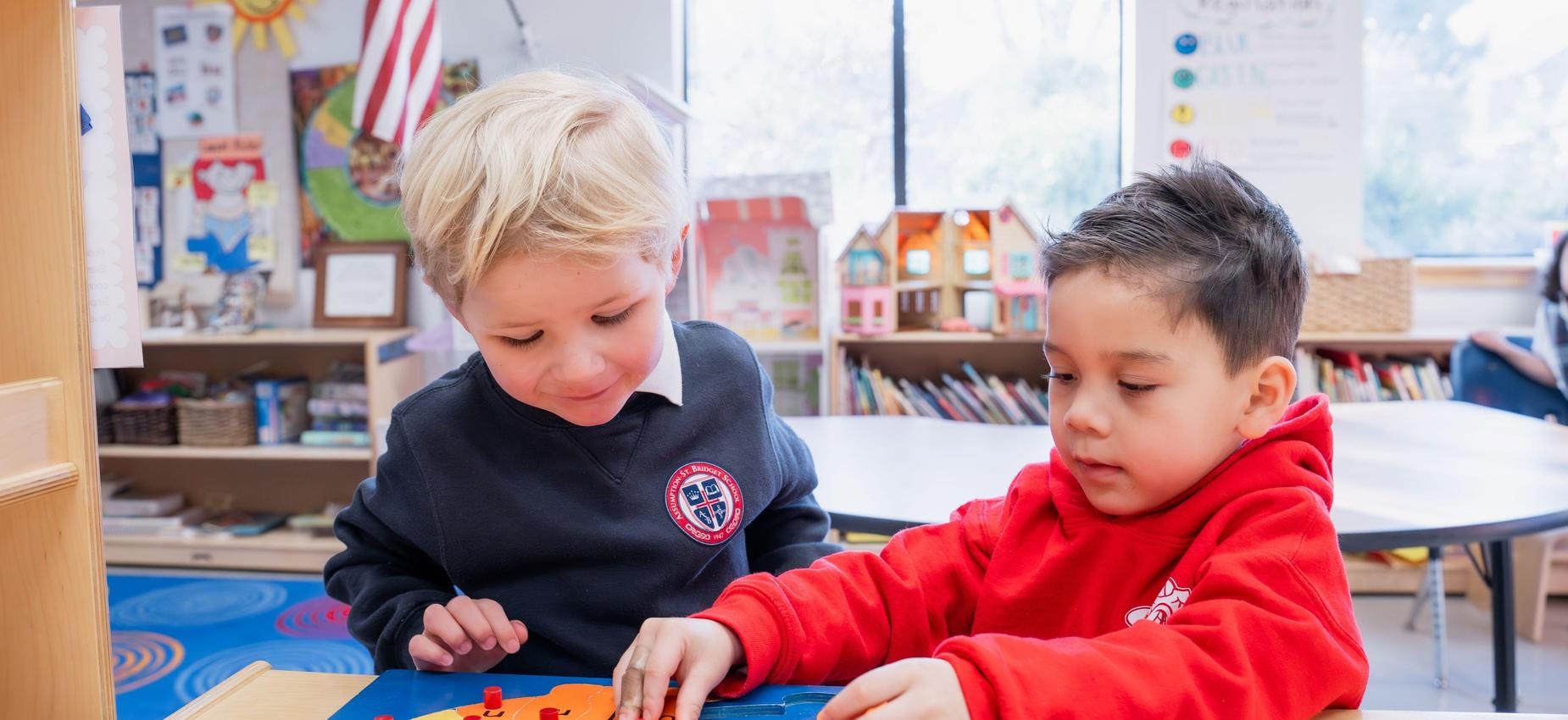 Two children playing with a puzzle or game at a table in a classroom