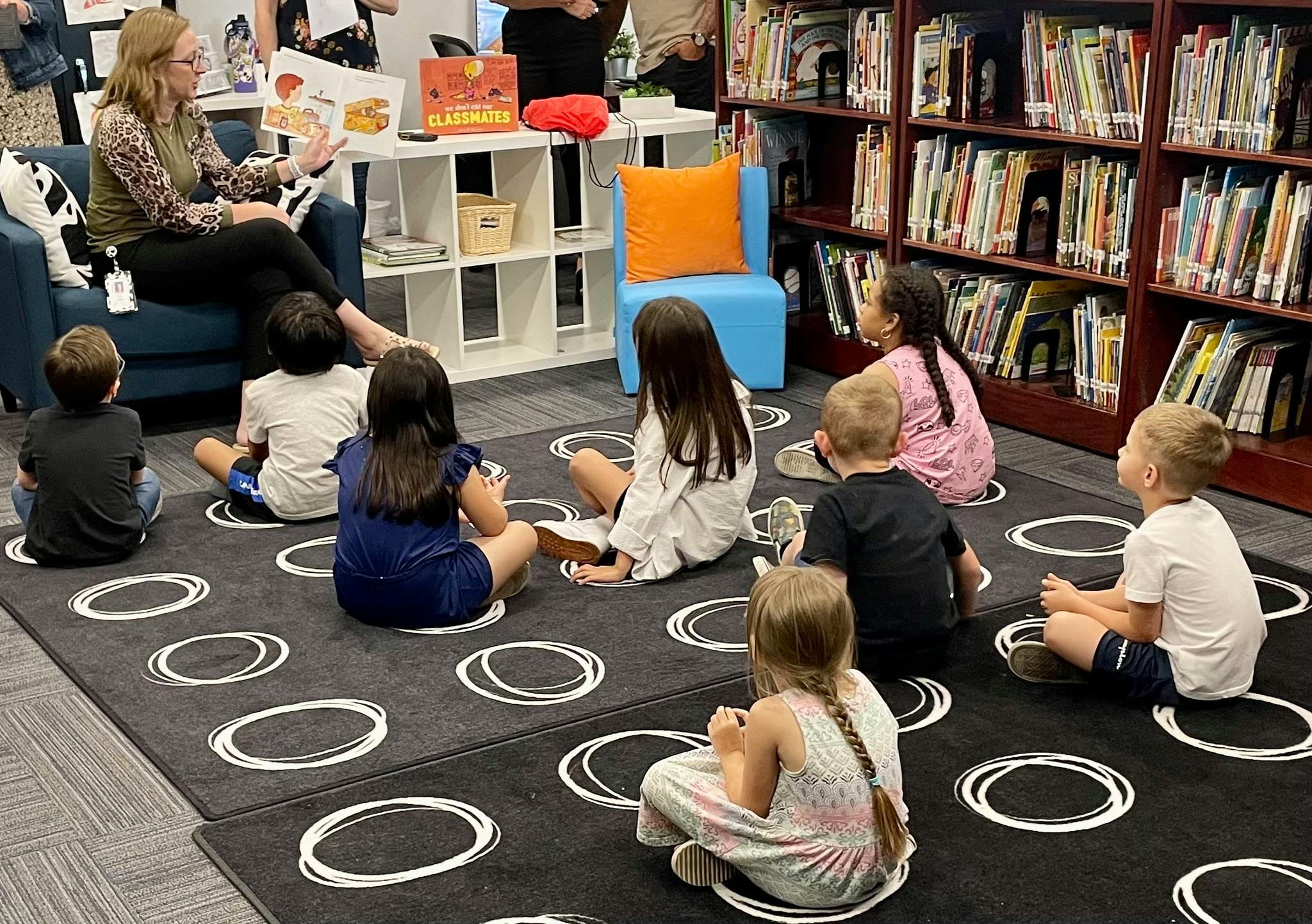 Person reading to a group of children sitting on a rug in a library