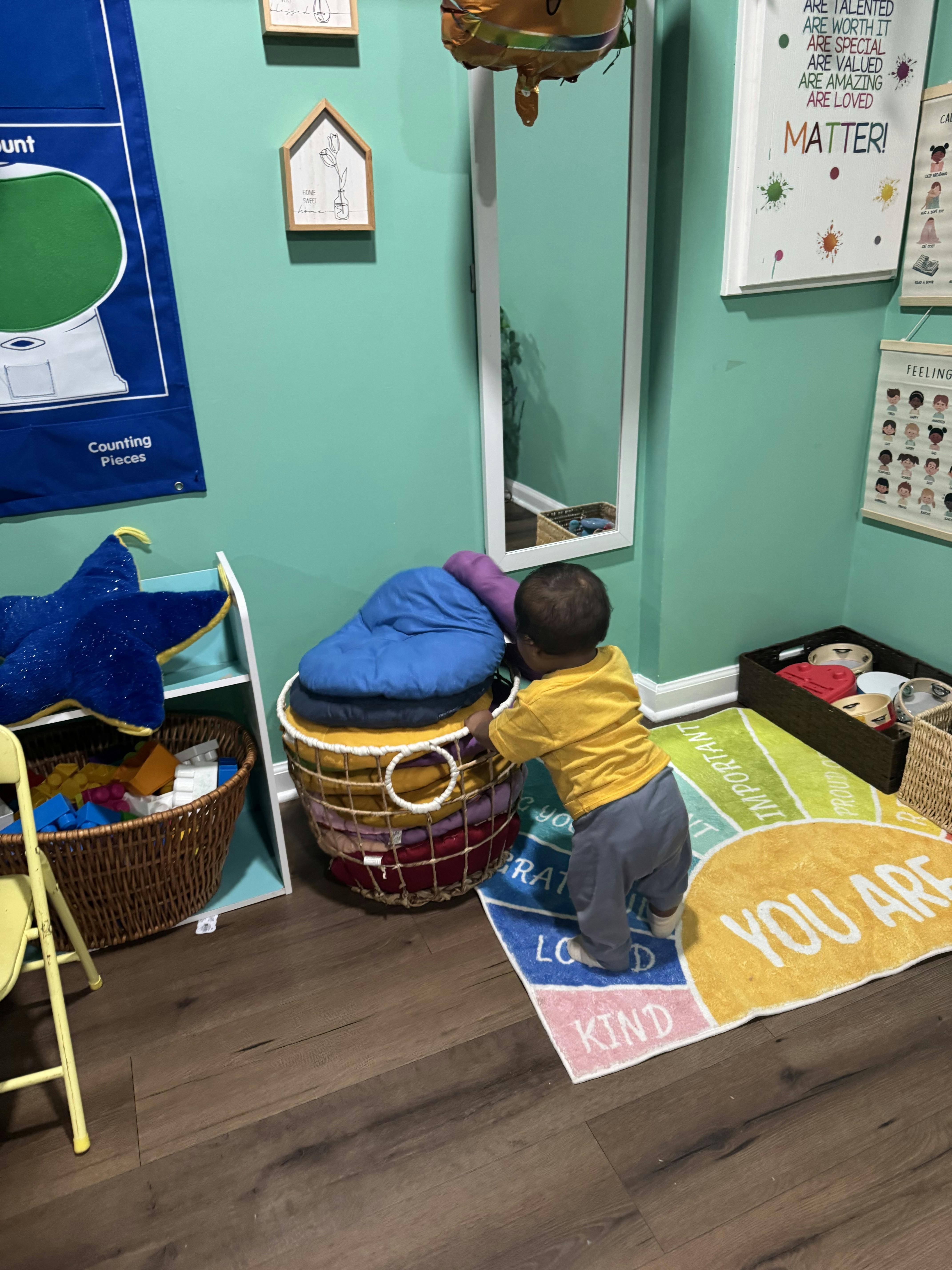 A toddler standing and holding onto a stack of cushions in a room