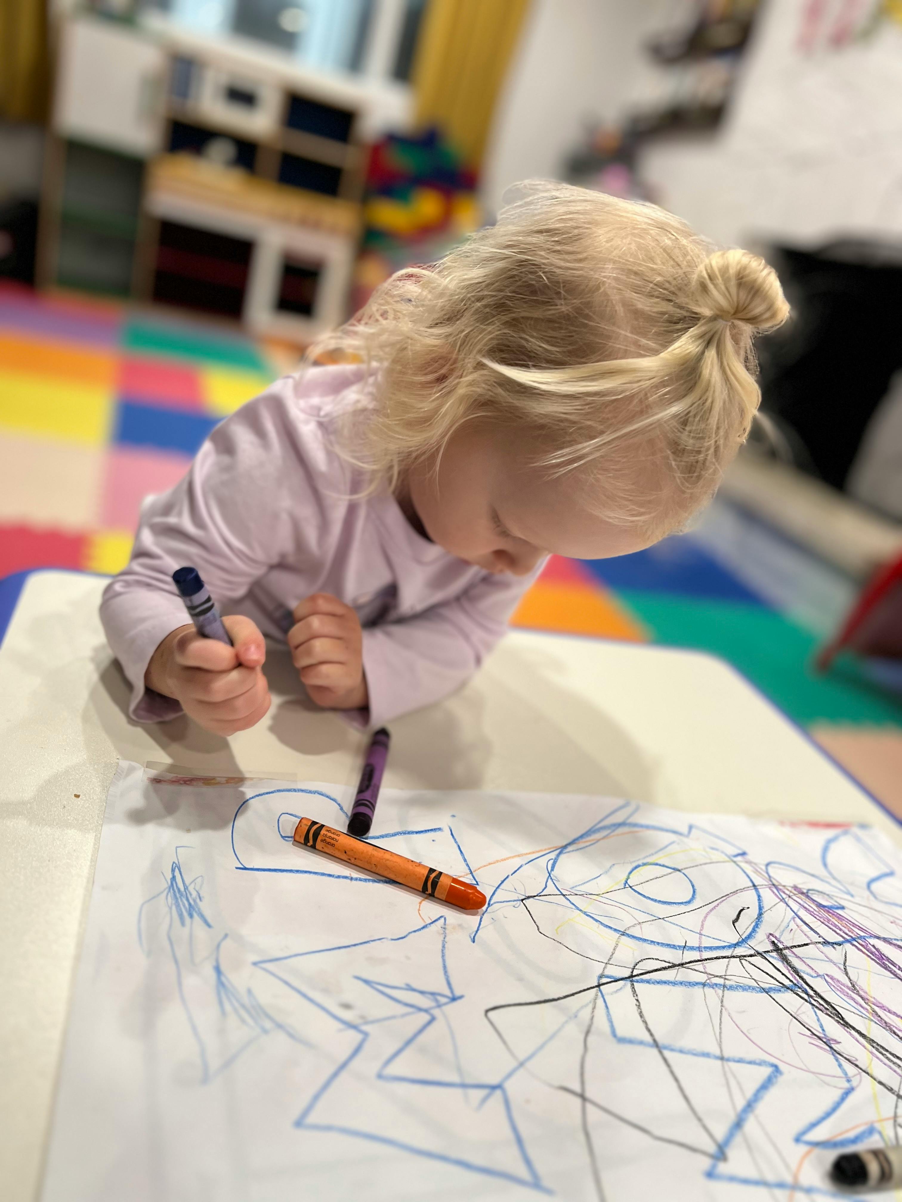 Child drawing on paper with crayons