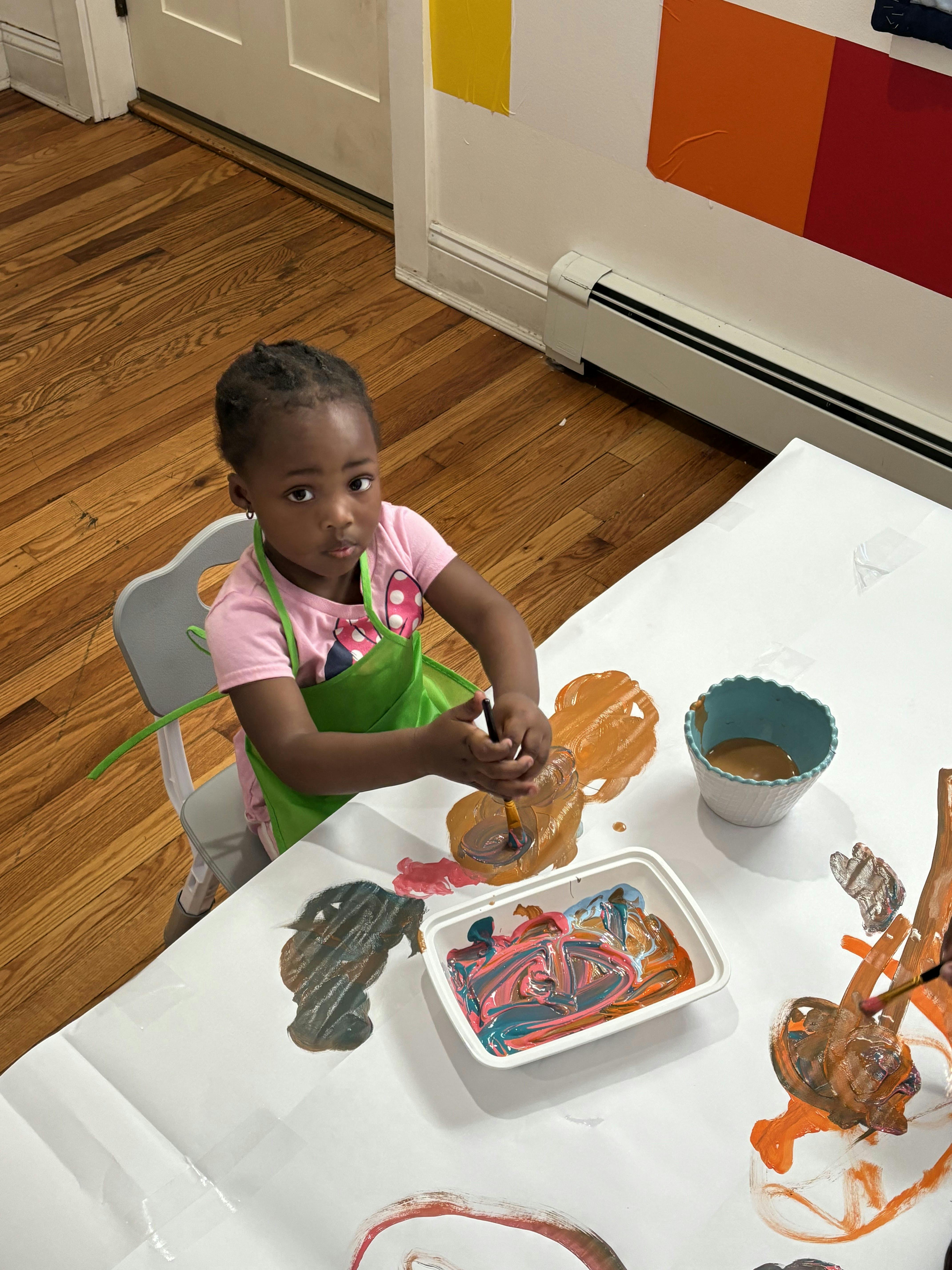 Child wearing an apron painting on white paper at a table