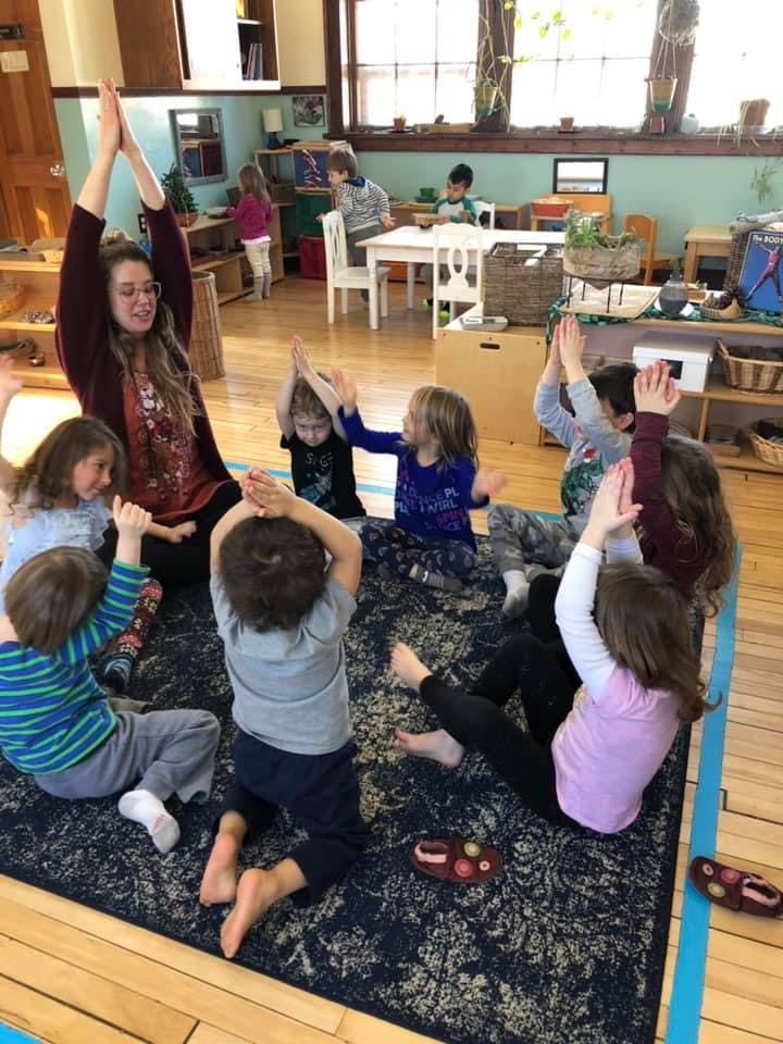 Adult and children sitting on a rug with arms raised