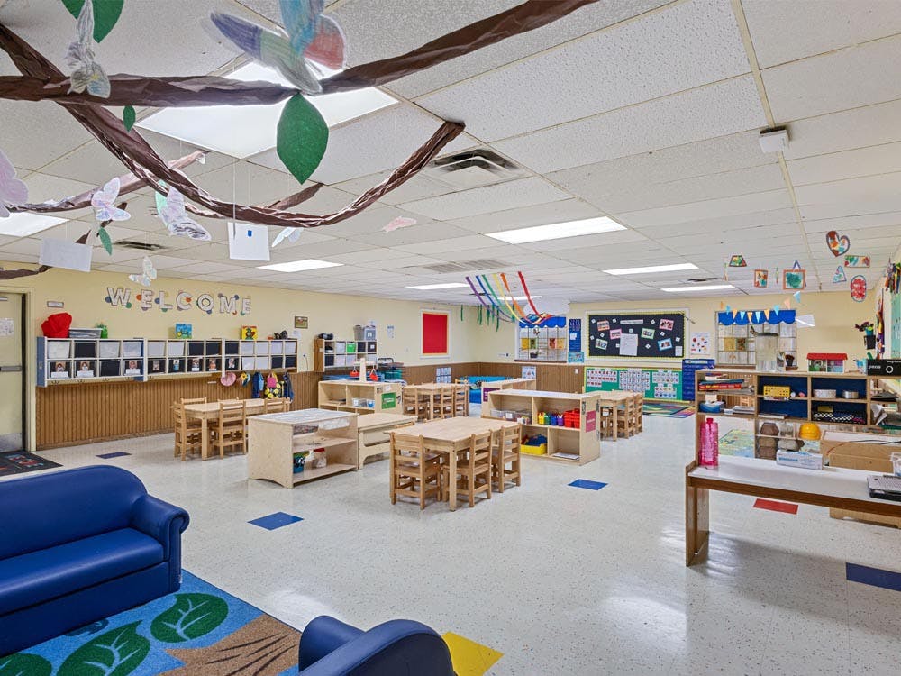 Classroom with small wooden tables and chairs, blue sofa, and decorations