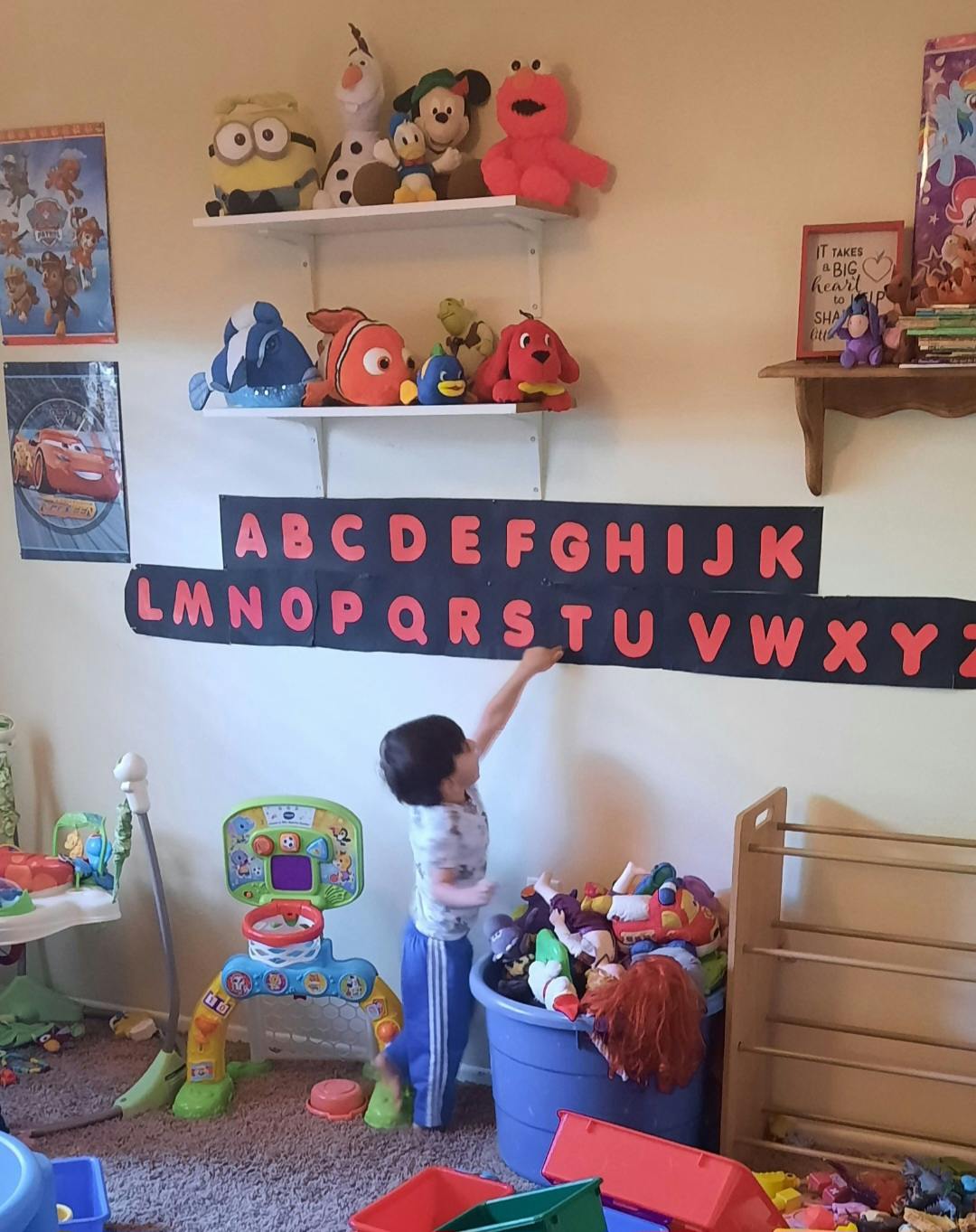 Child pointing to alphabet letters on a wall in a playroom