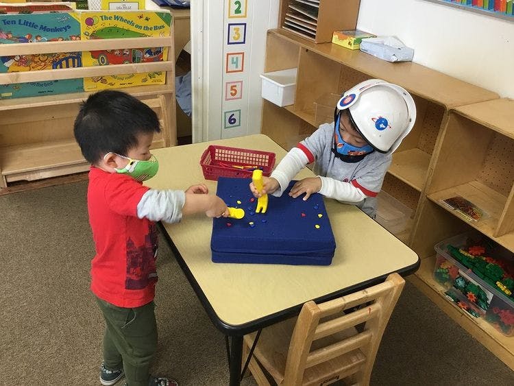 Two children playing with toys at a table in a classroom
