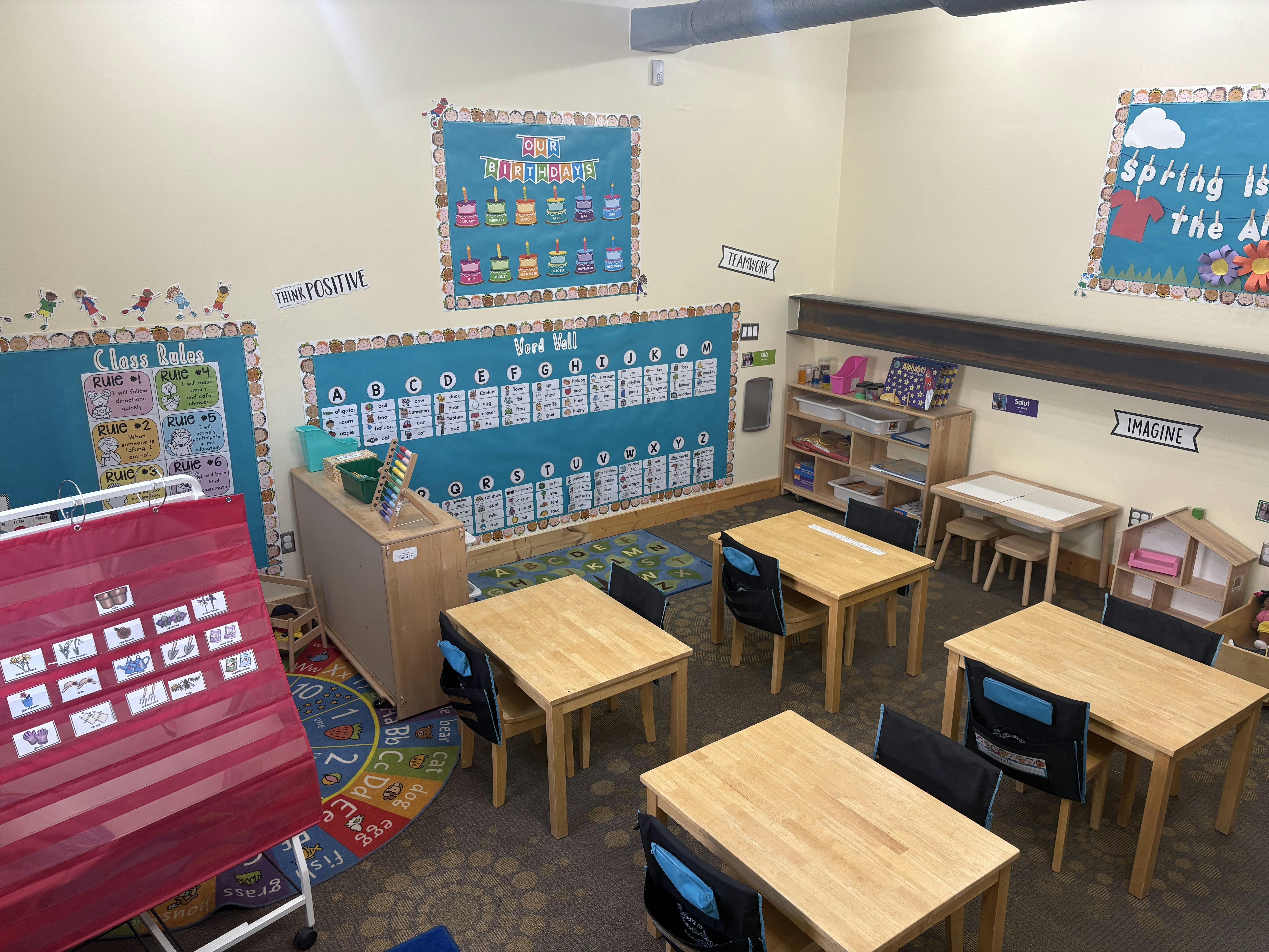 Classroom with wooden tables and chairs, alphabet and rule charts on walls