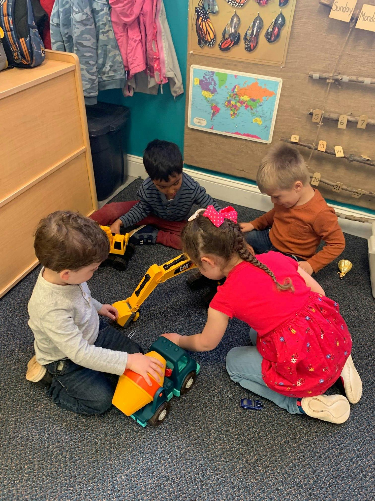 Four children playing with toy construction vehicles on the floor