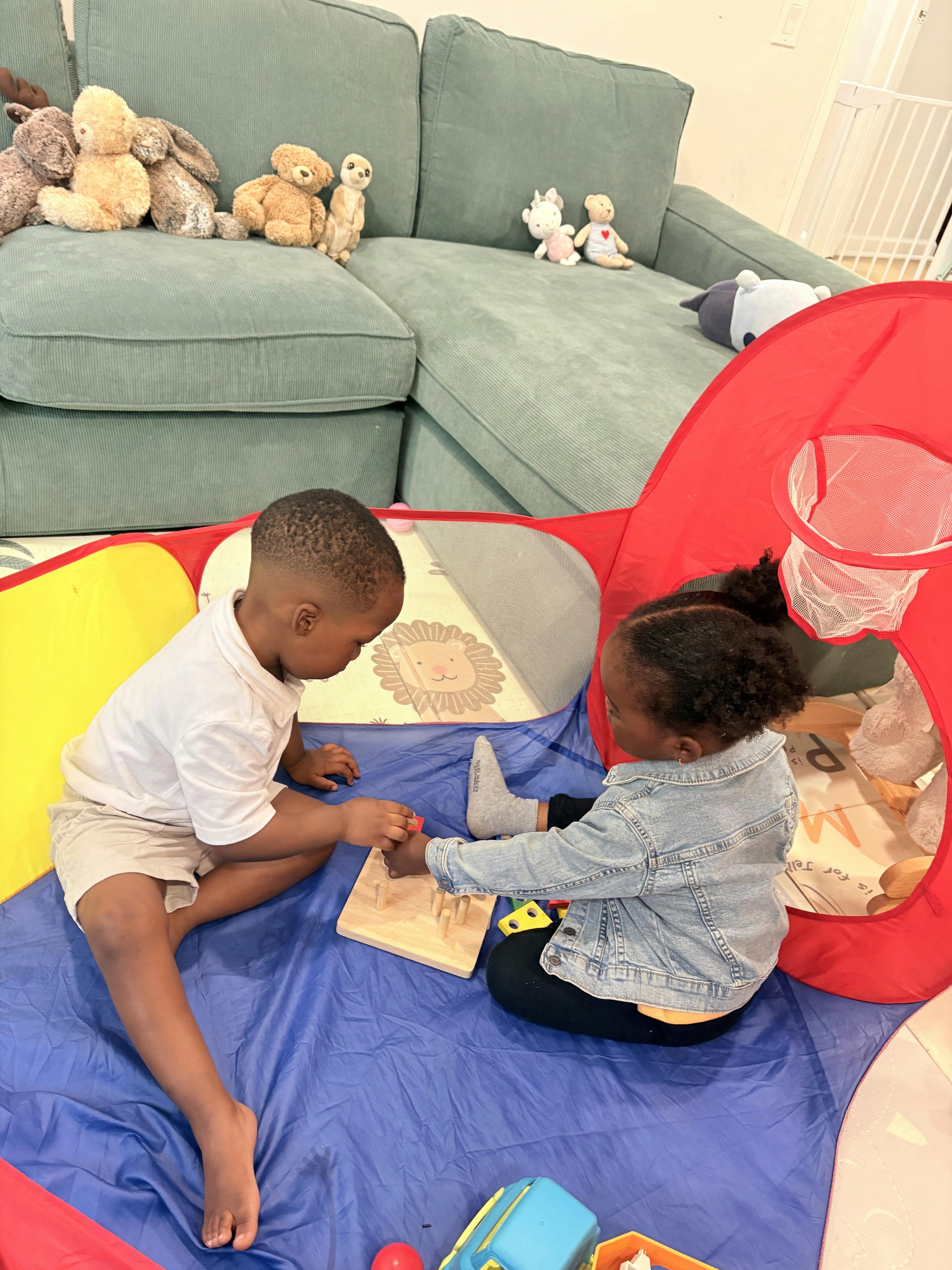 Two children playing with a wooden peg puzzle inside a pop-up play tent