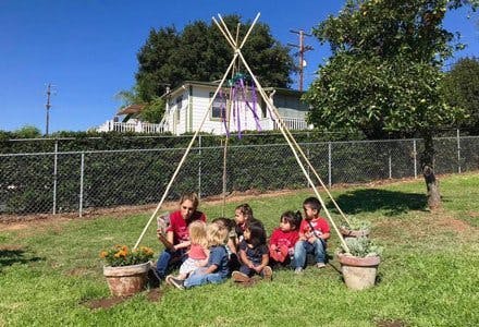 Adult reading to children sitting under a teepee structure outdoors