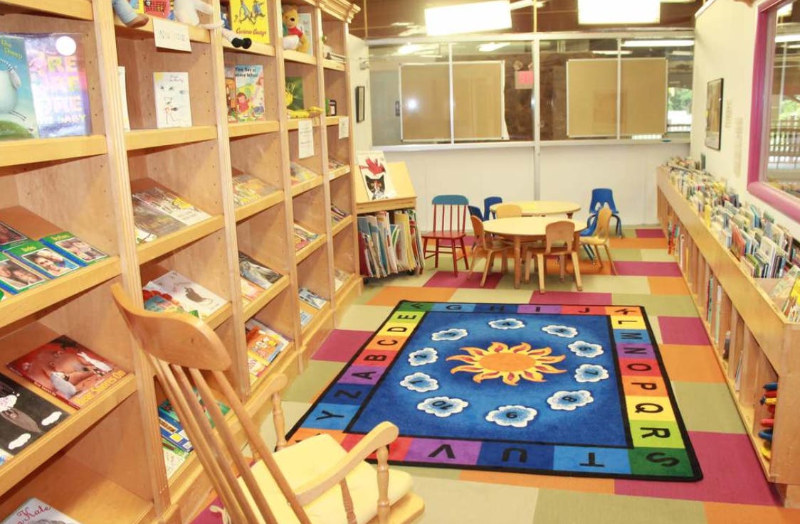 Children's library with bookshelves, small tables and chairs, and a colorful rug