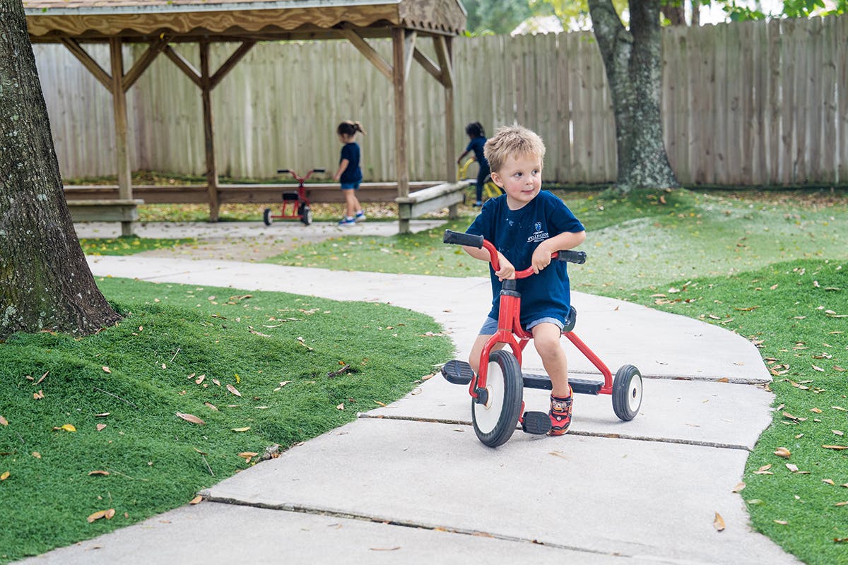 Child riding a red tricycle on a paved path outdoors