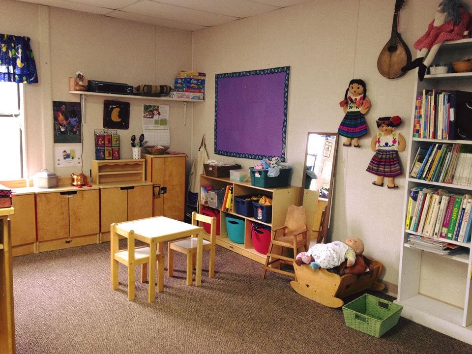 Classroom with small tables and chairs, shelves with books and toys