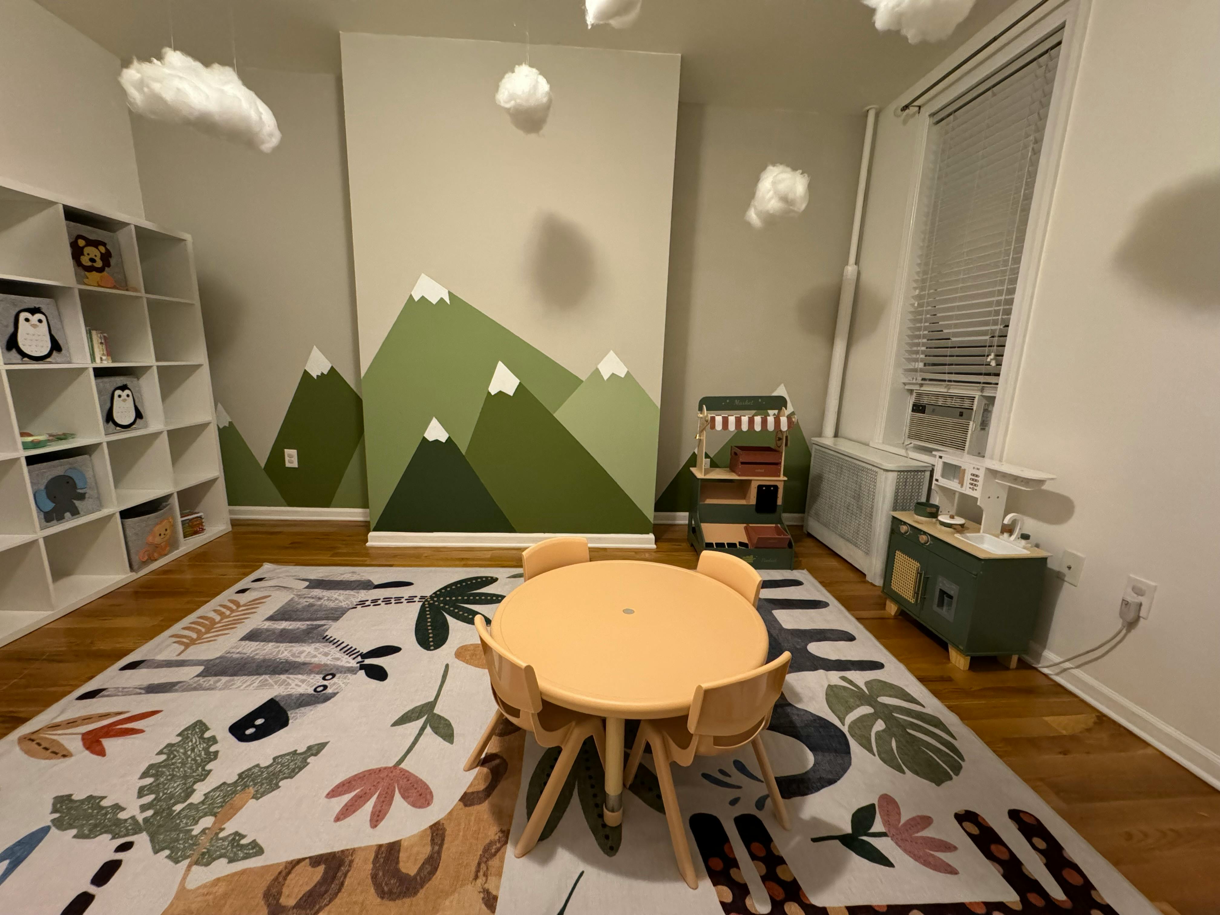 Playroom with mountain mural, small table and chairs, and toy shelves