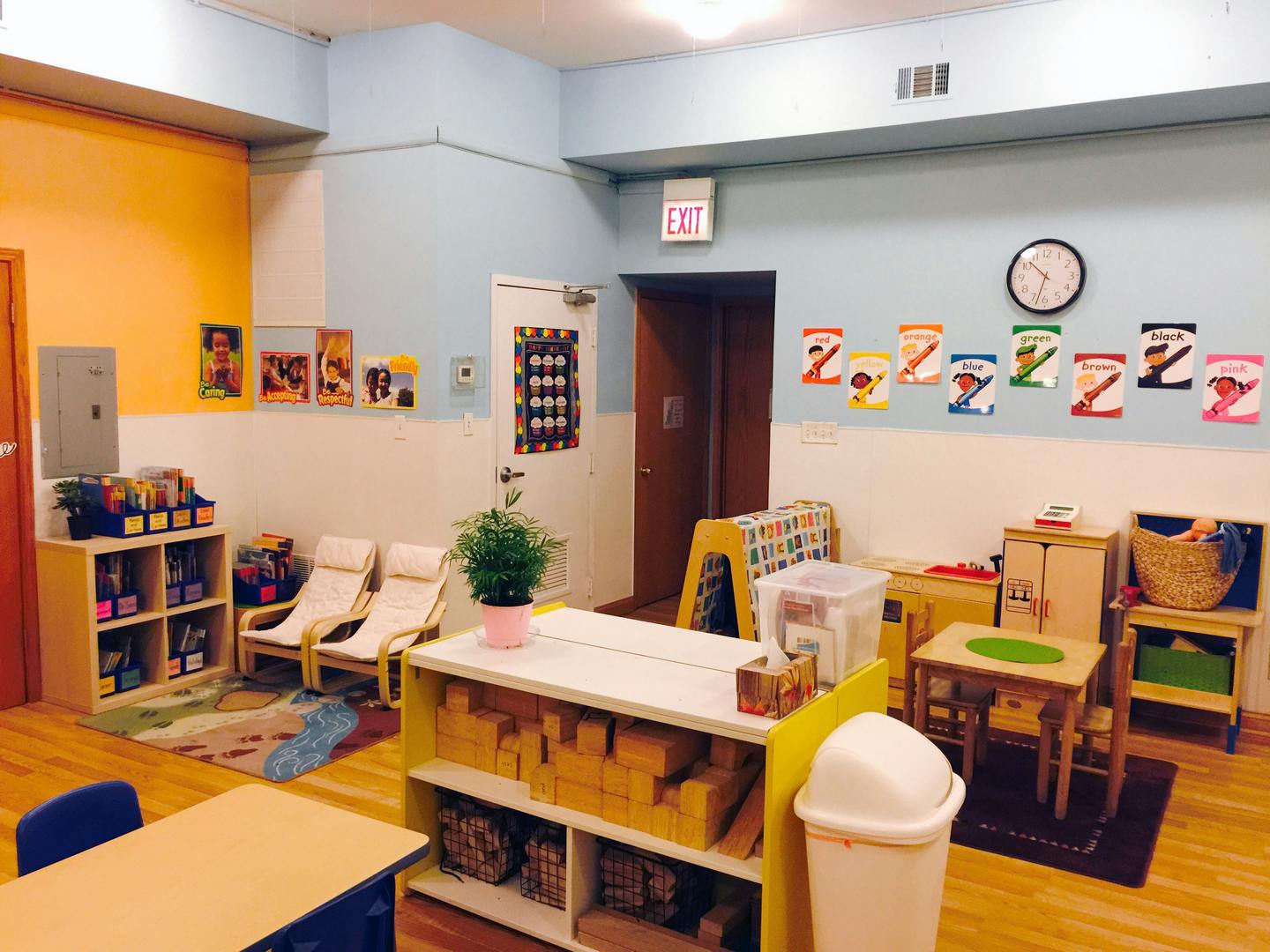 Classroom with small tables, chairs, shelves, and an exit sign