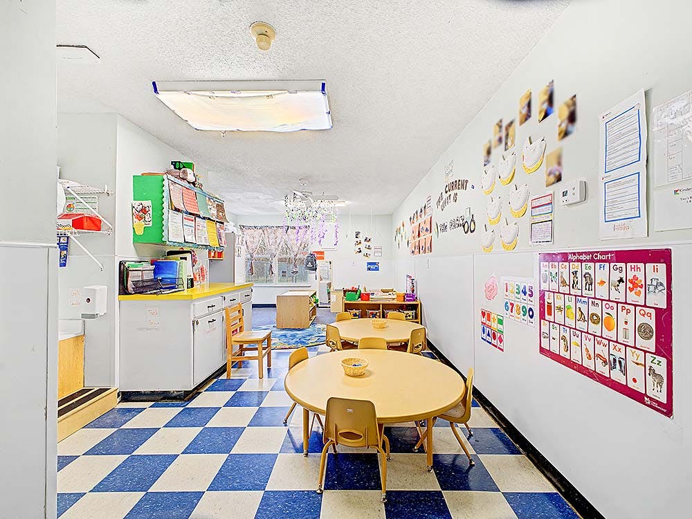 Empty classroom with small tables and chairs, alphabet chart on wall