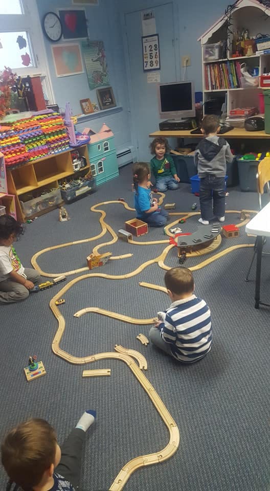 Children playing with a wooden train set on a classroom floor