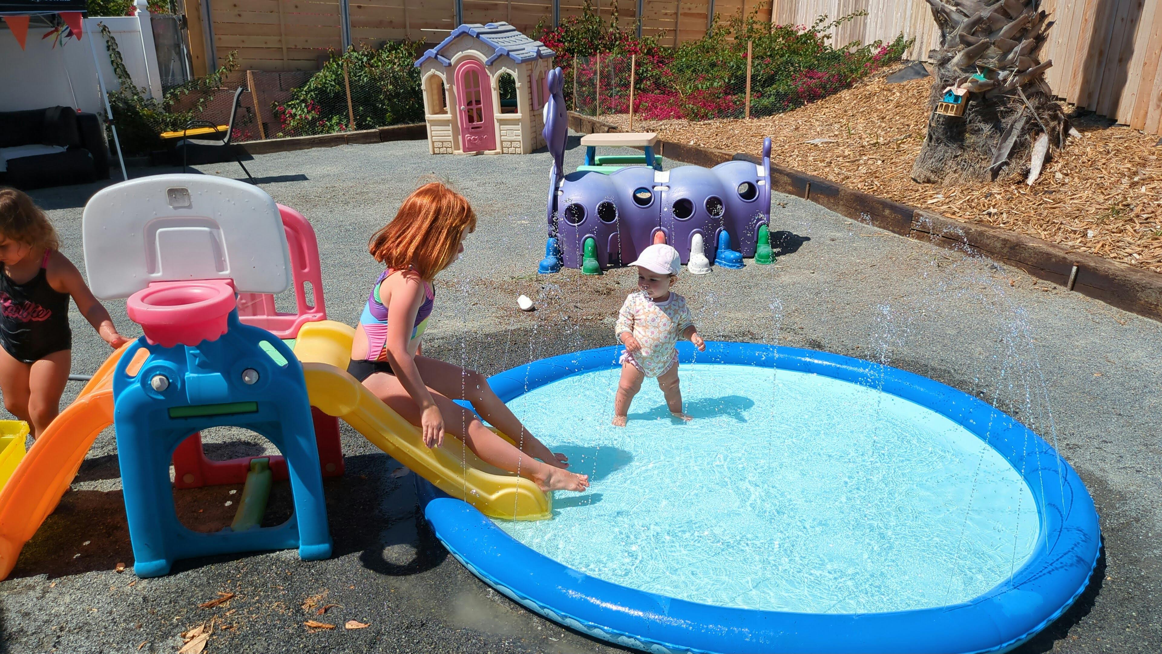 Child on a slide next to a wading pool with another child standing in it