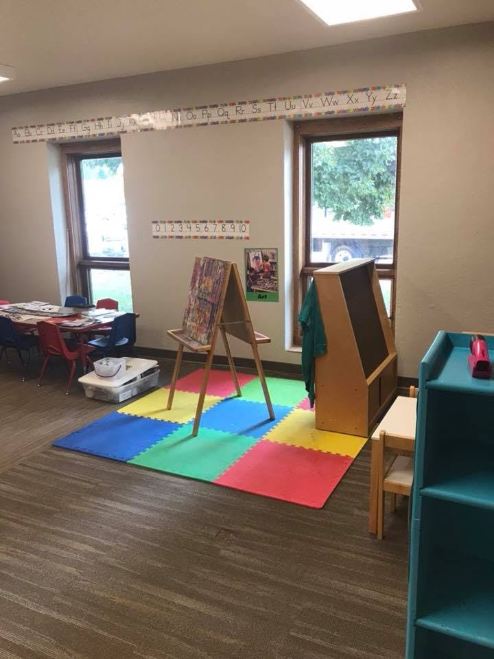 Classroom with colorful floor mats, easel, and tables