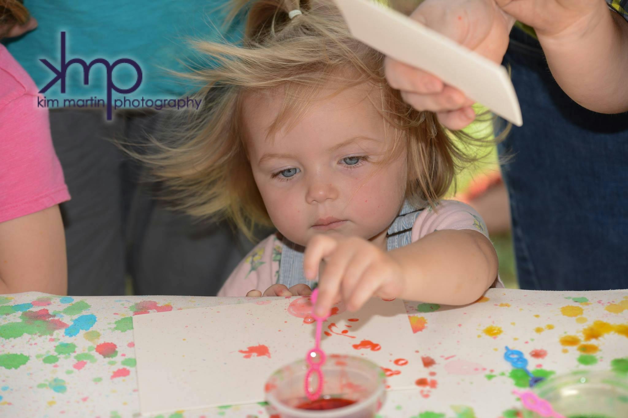 Child blowing bubbles into a cup of red liquid