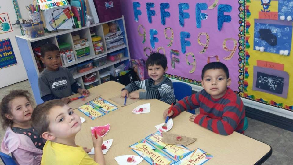 Four children sitting at a table with papers and craft supplies